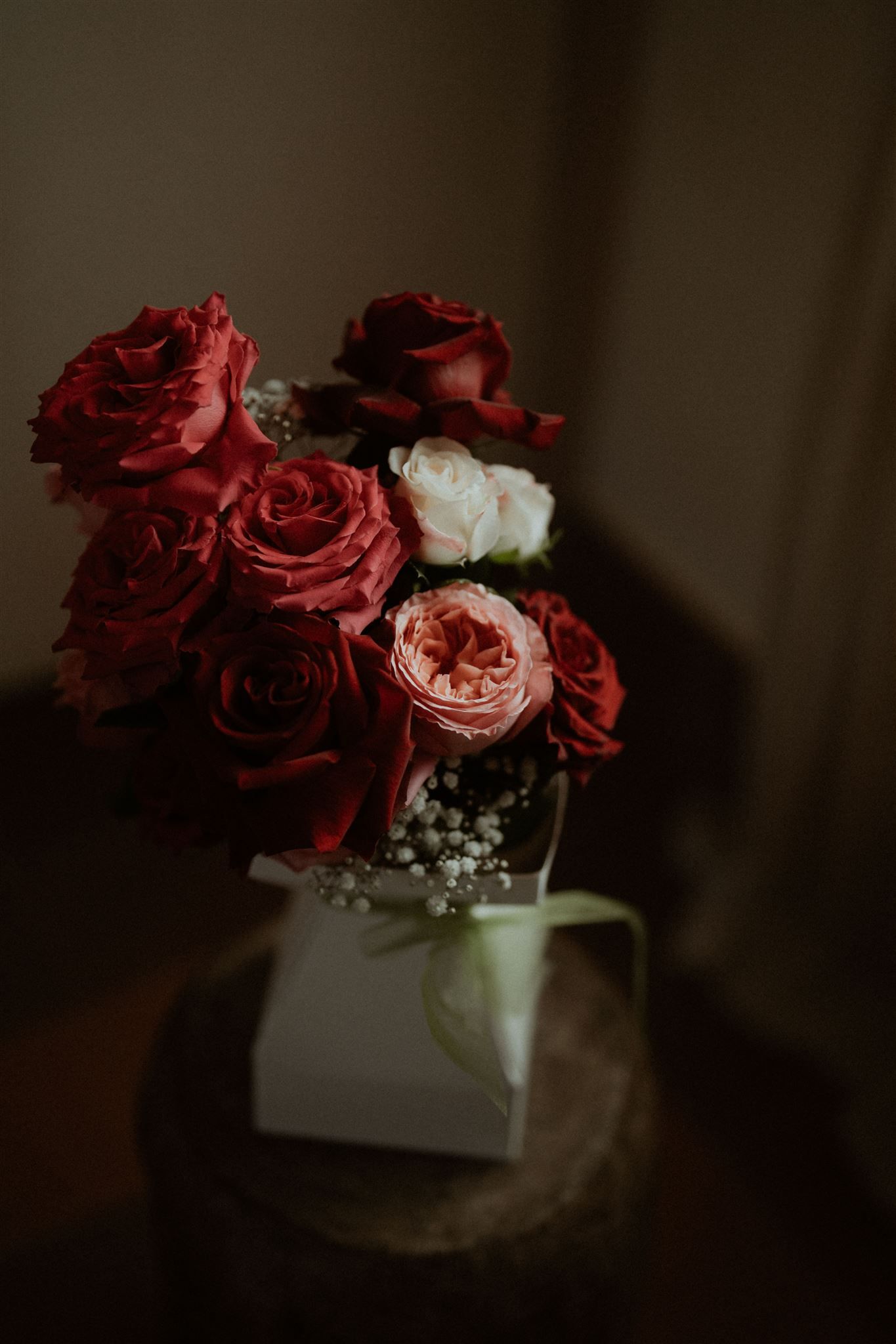 Bouquet of red and pink roses and white flowers in a white box with a green ribbon, on a wooden surface.