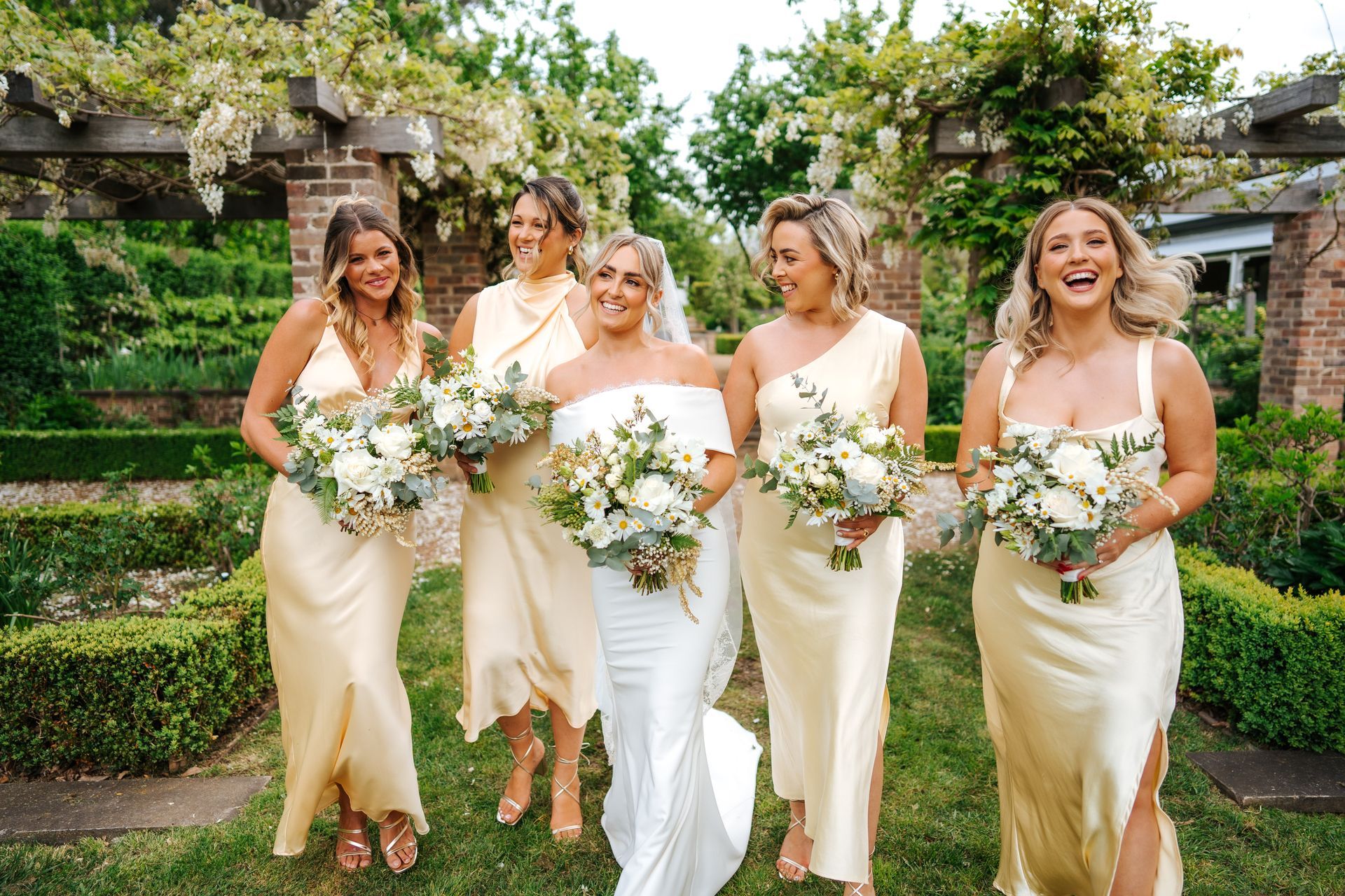 Bride in white dress with bridesmaids in yellow dresses, smiling in a garden.