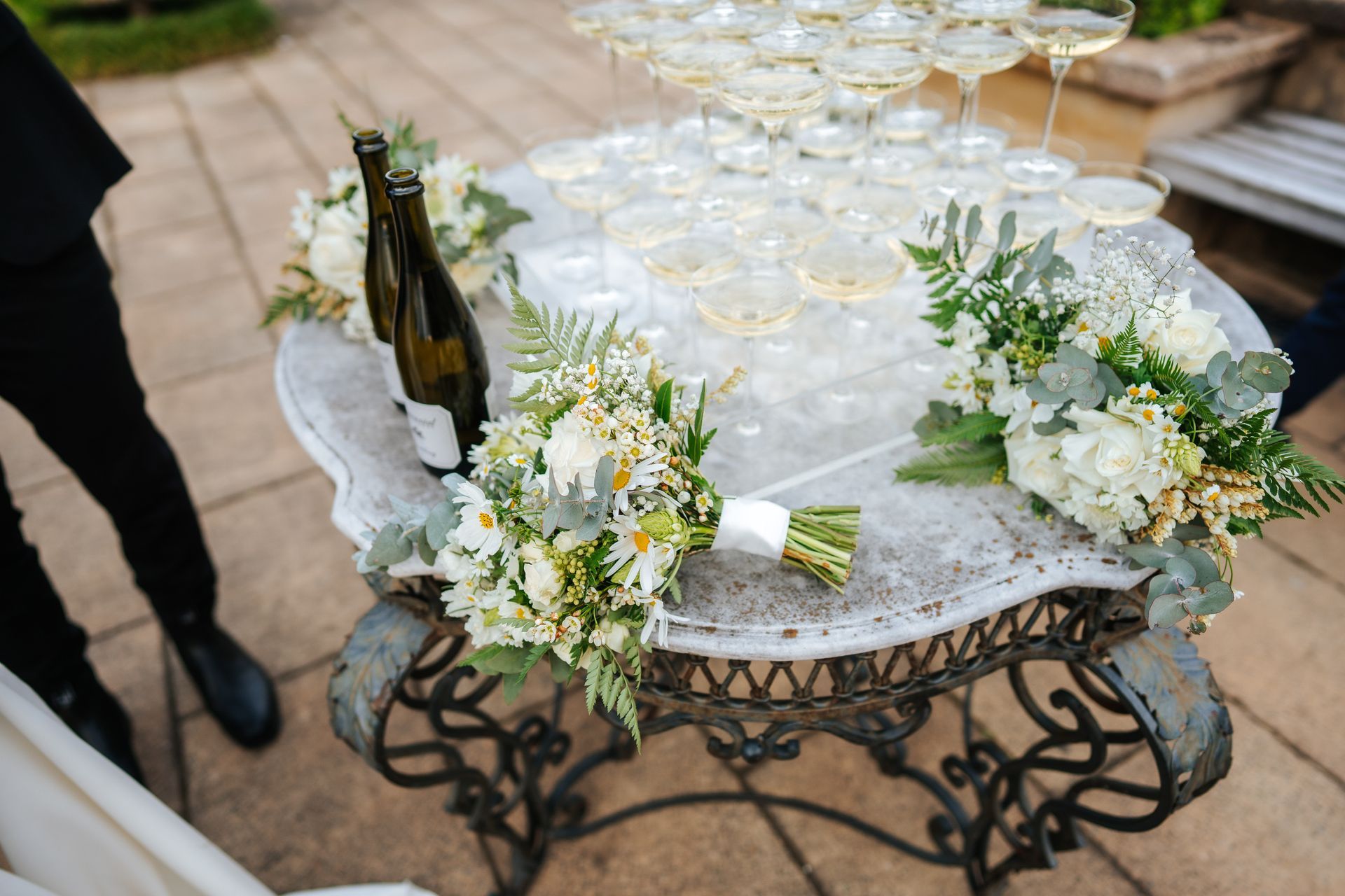 Champagne glasses in a pyramid on a table, floral bouquets, bottle of wine, event setting.