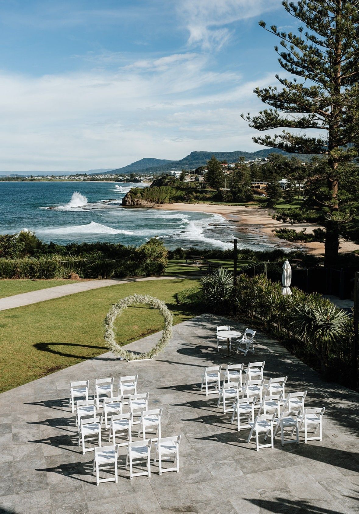 Wedding ceremony setup overlooking the ocean, white chairs arranged around floral arch.