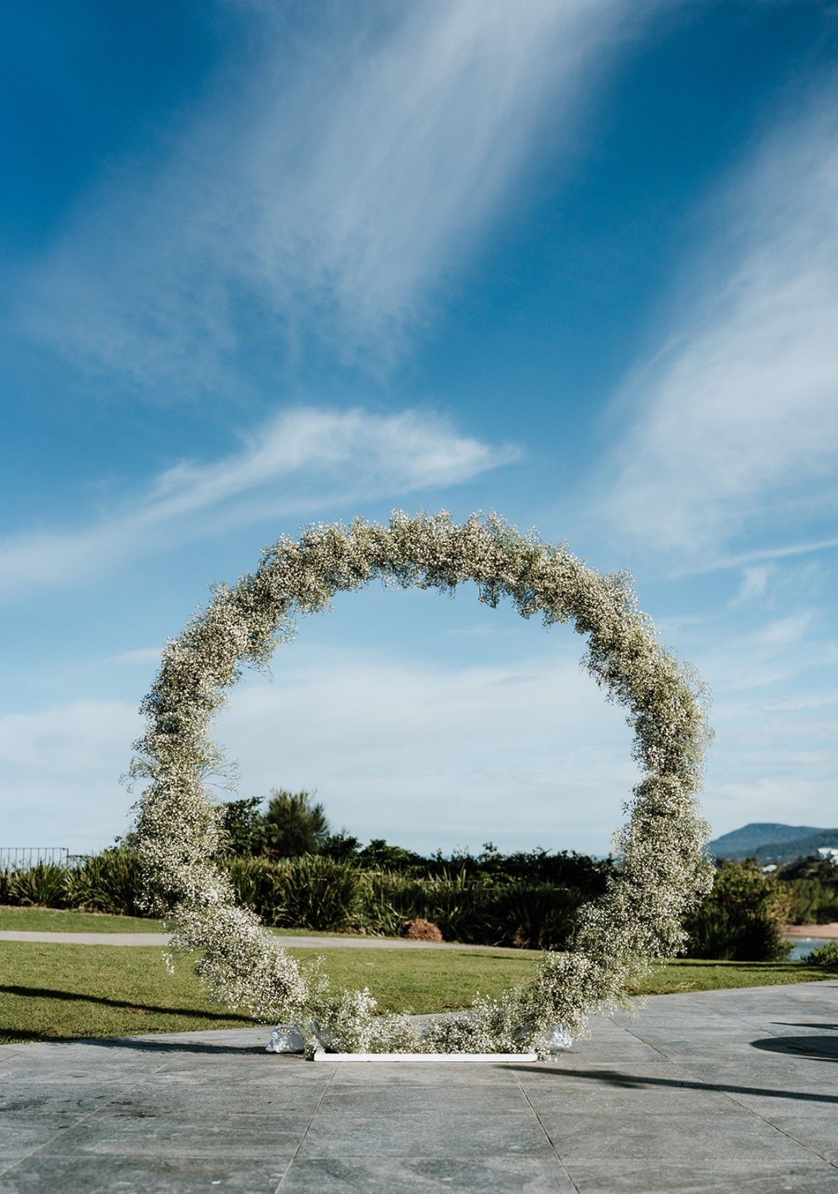 Floral-covered circular wedding arch on a grassy lawn under a blue sky.