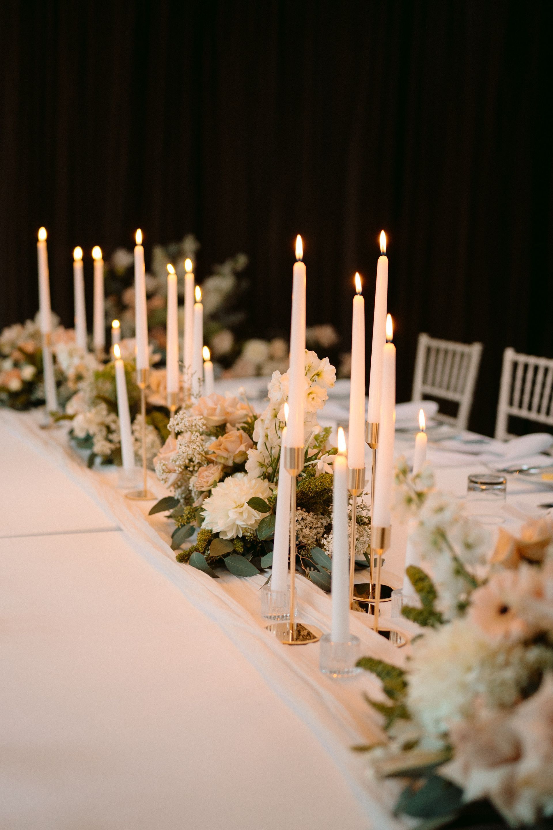 Long table set for a formal event with lit candles and floral arrangements.