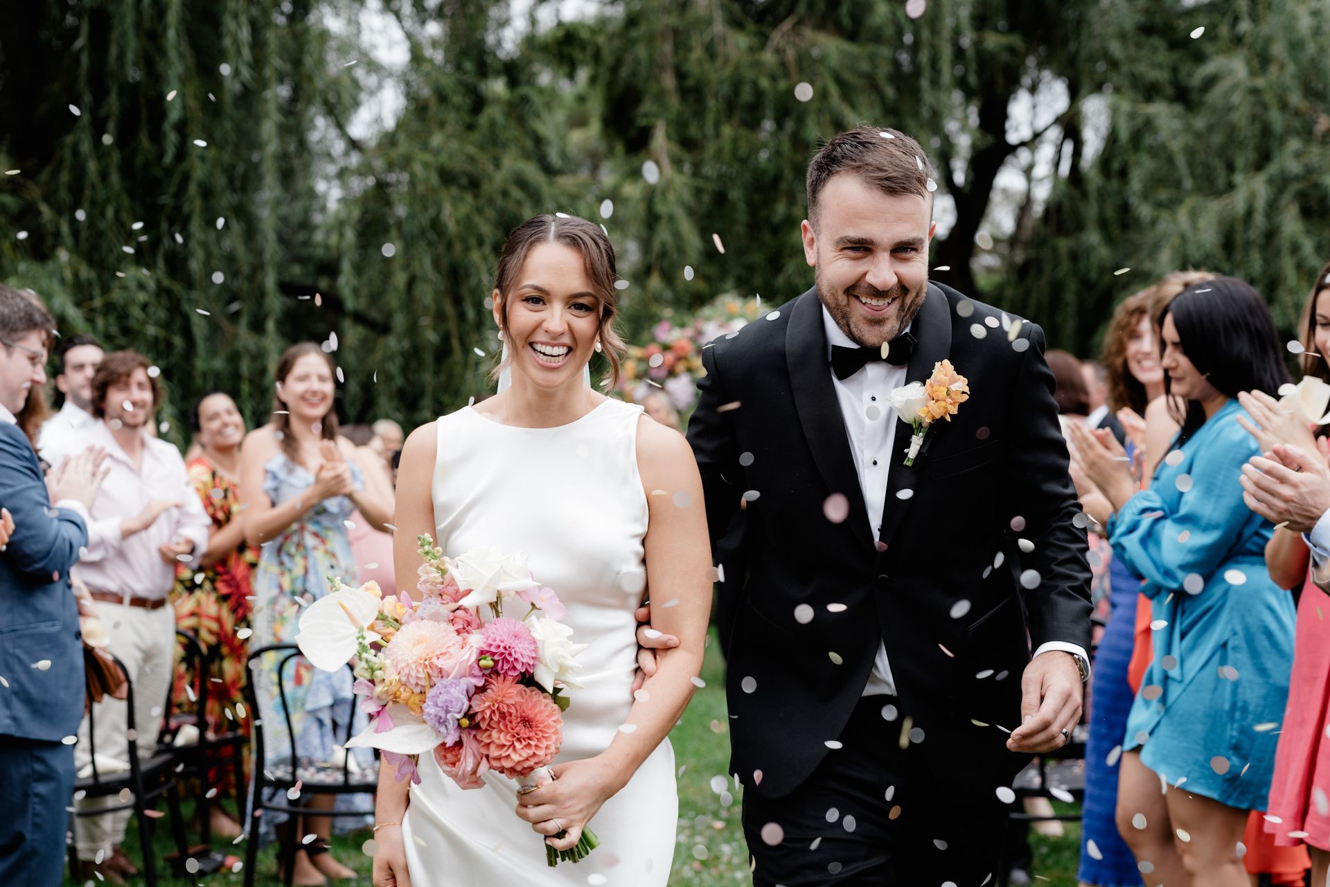 Bride and groom smiling, walking through confetti after wedding ceremony.