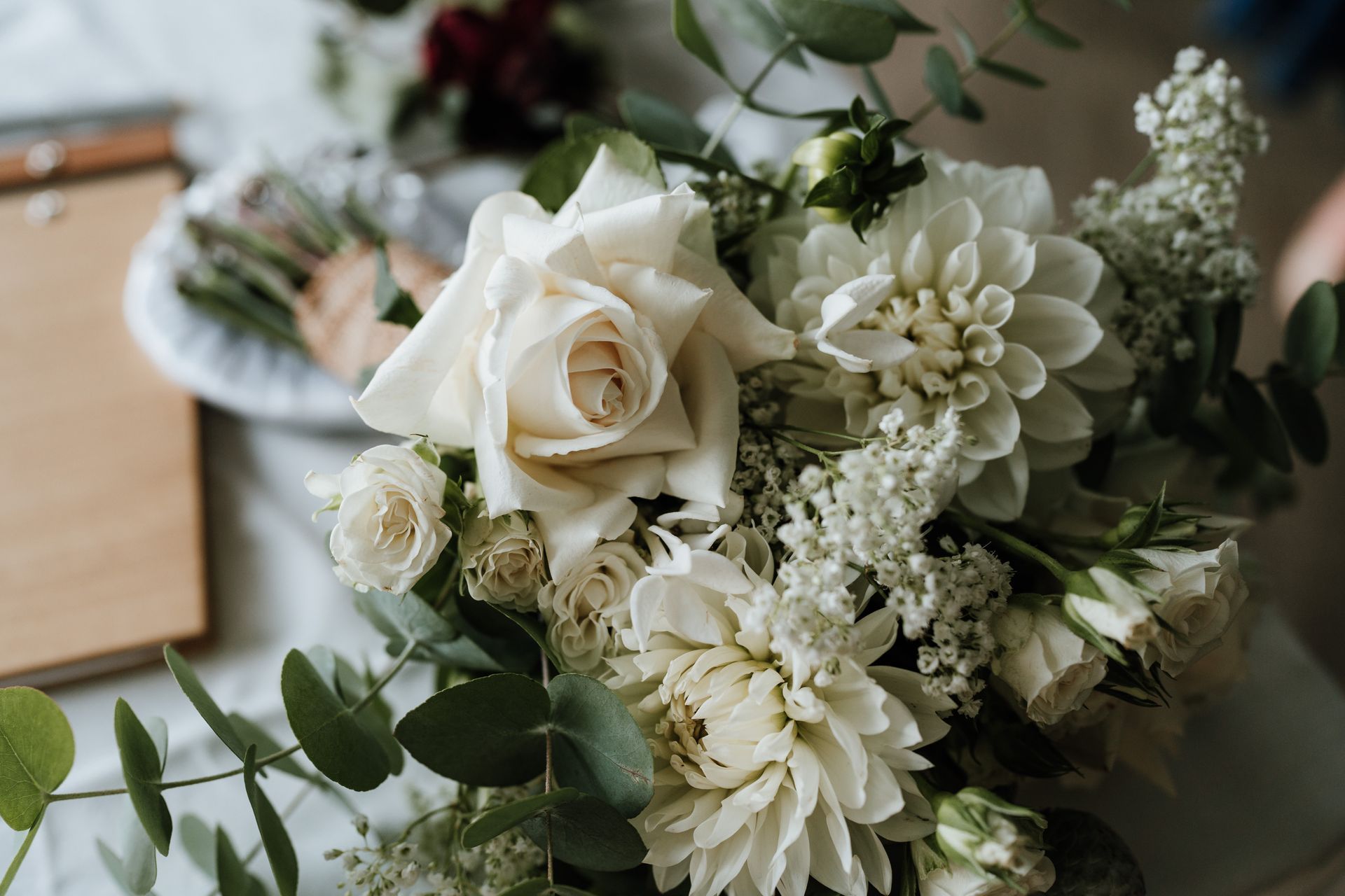 Close-up of a white floral arrangement with roses, dahlias, and greenery on a light surface.
