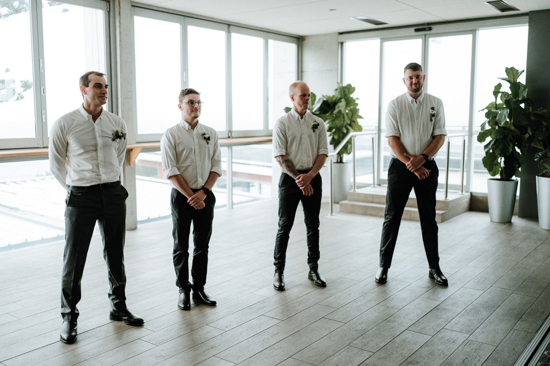 Four men in formal attire stand indoors; sunlight floods the room.