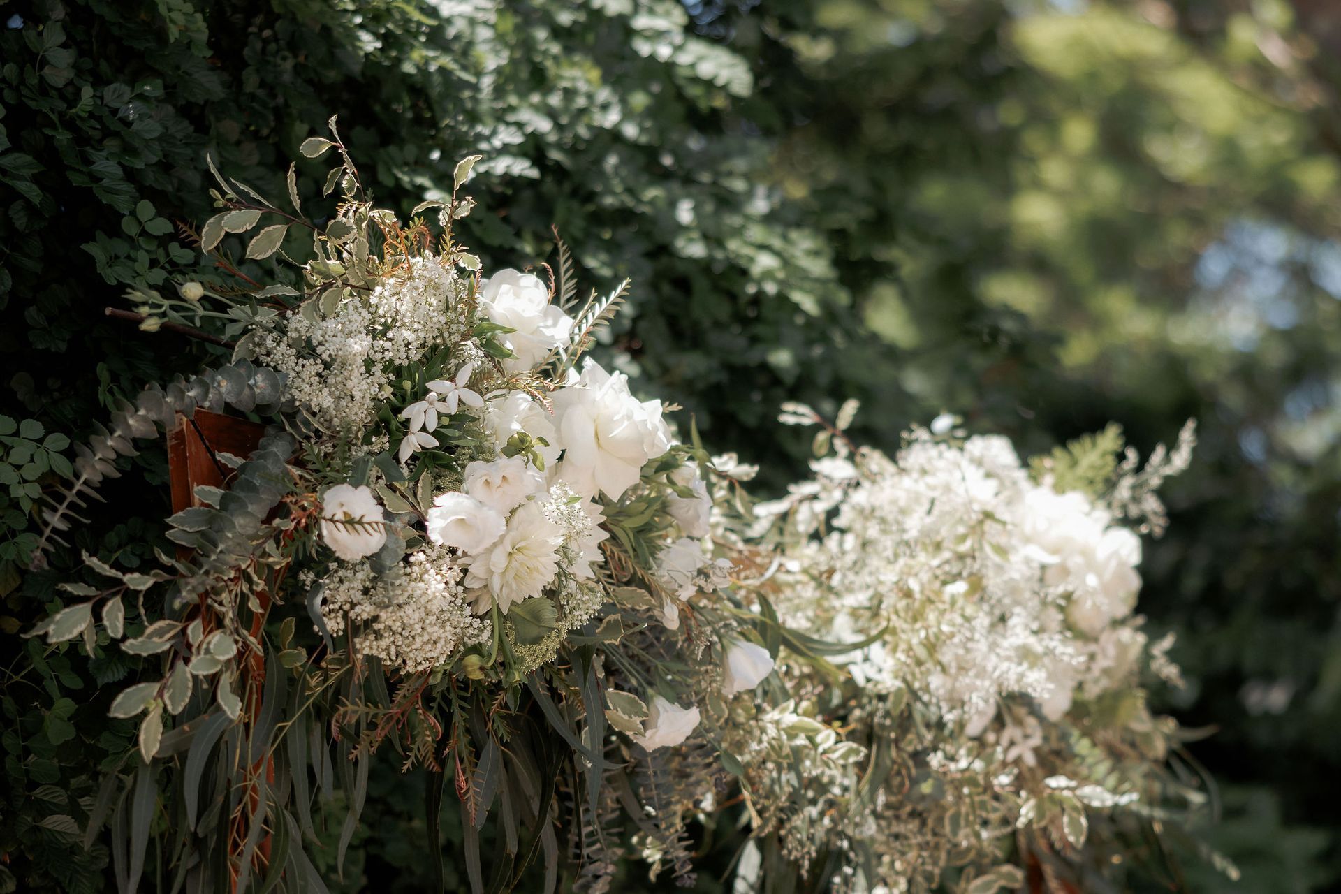 White floral arrangements on a wooden structure against a background of green foliage, in a bright outdoor setting.