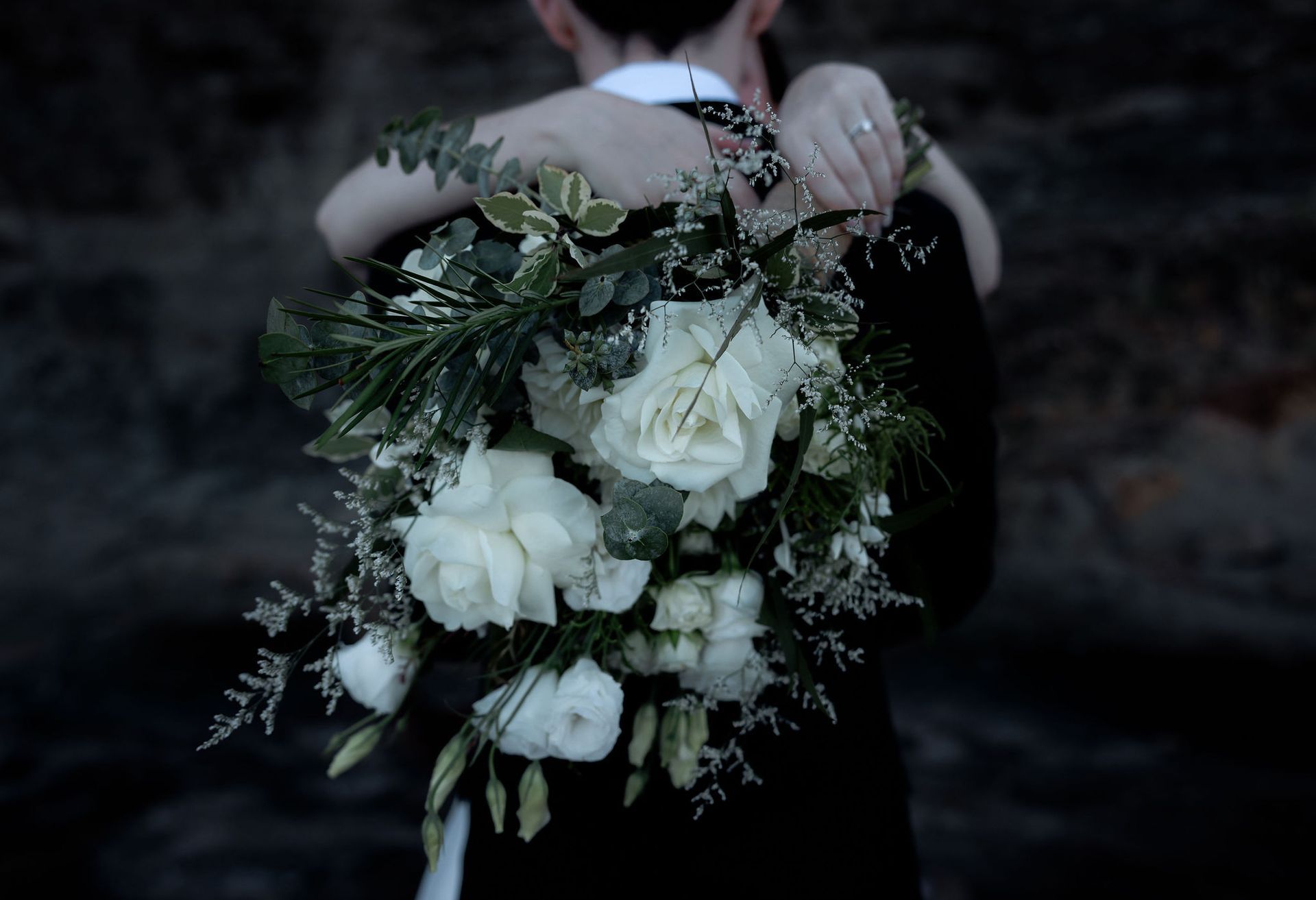 Couple embracing, bouquet of white roses in the foreground; dark background.