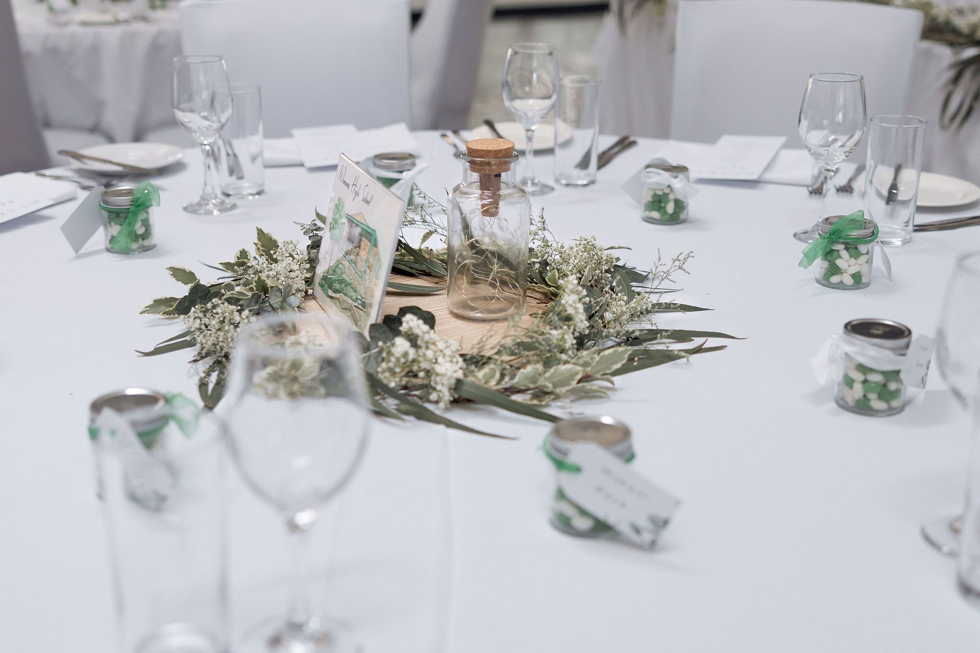 Wedding table setting with floral centerpiece, wine glasses, and favors.