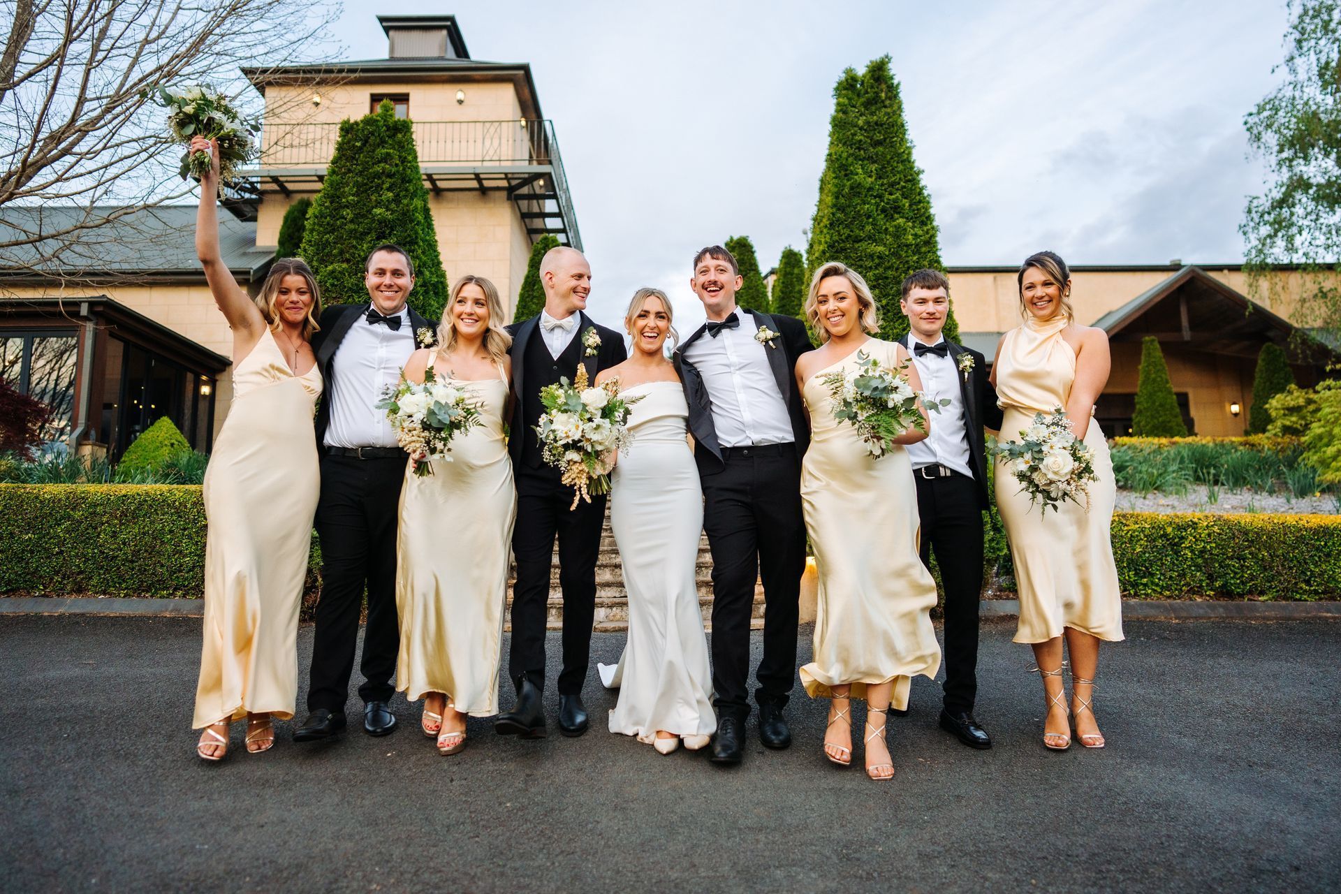 Wedding party: bride and groom with bridesmaids and groomsmen, smiling outside a building.