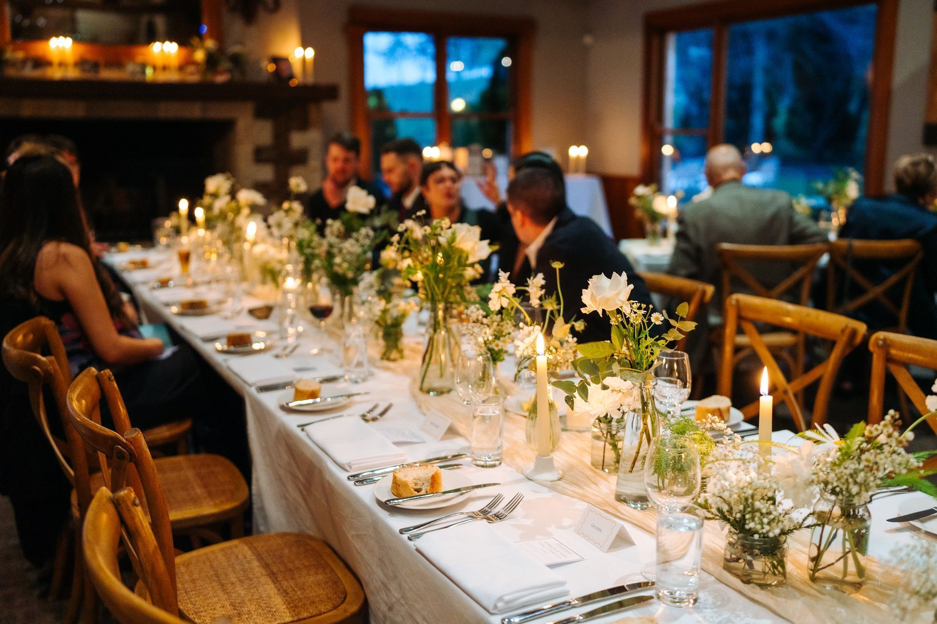 Long table set for dinner party with white flowers, candles, and guests.