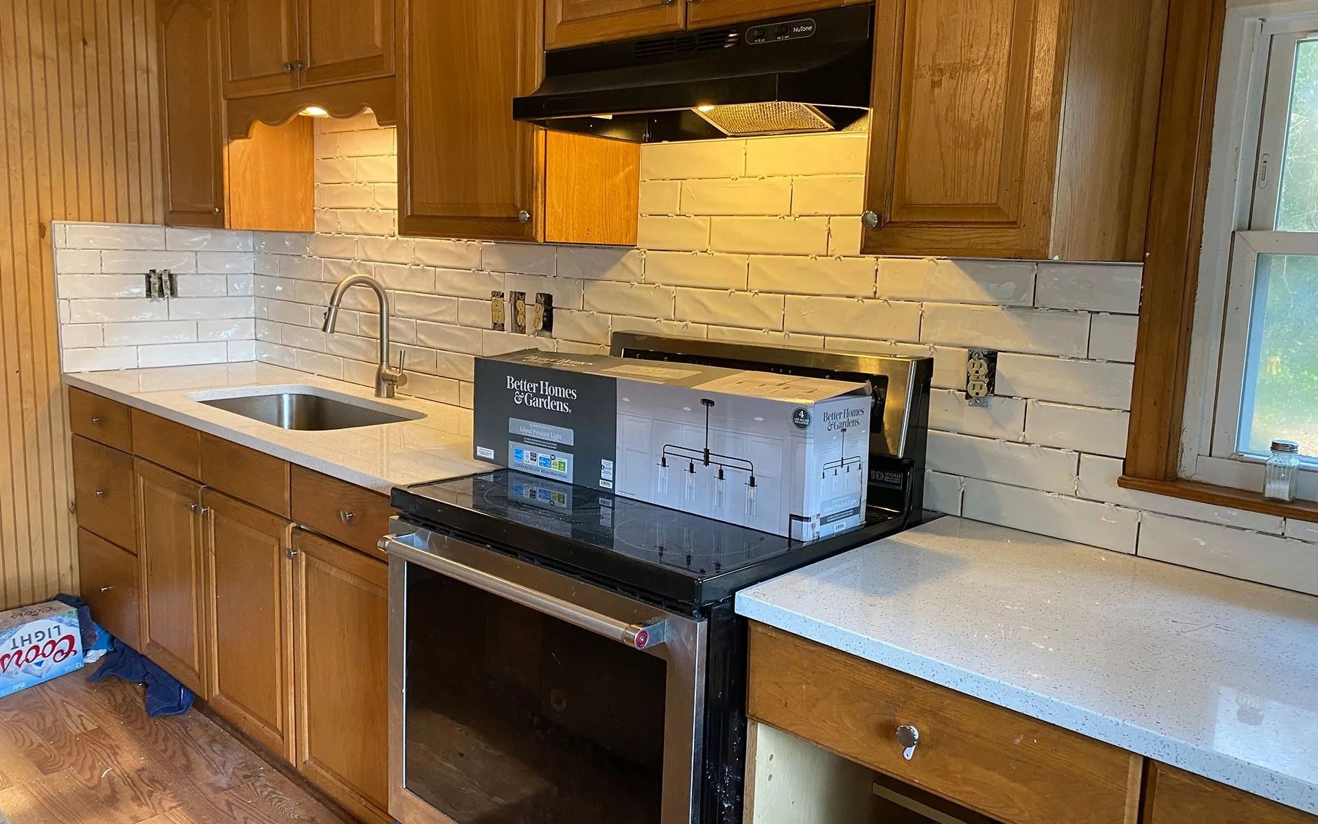 Kitchen with wooden cabinets, white brick backsplash, black stove, and white countertop under a window.