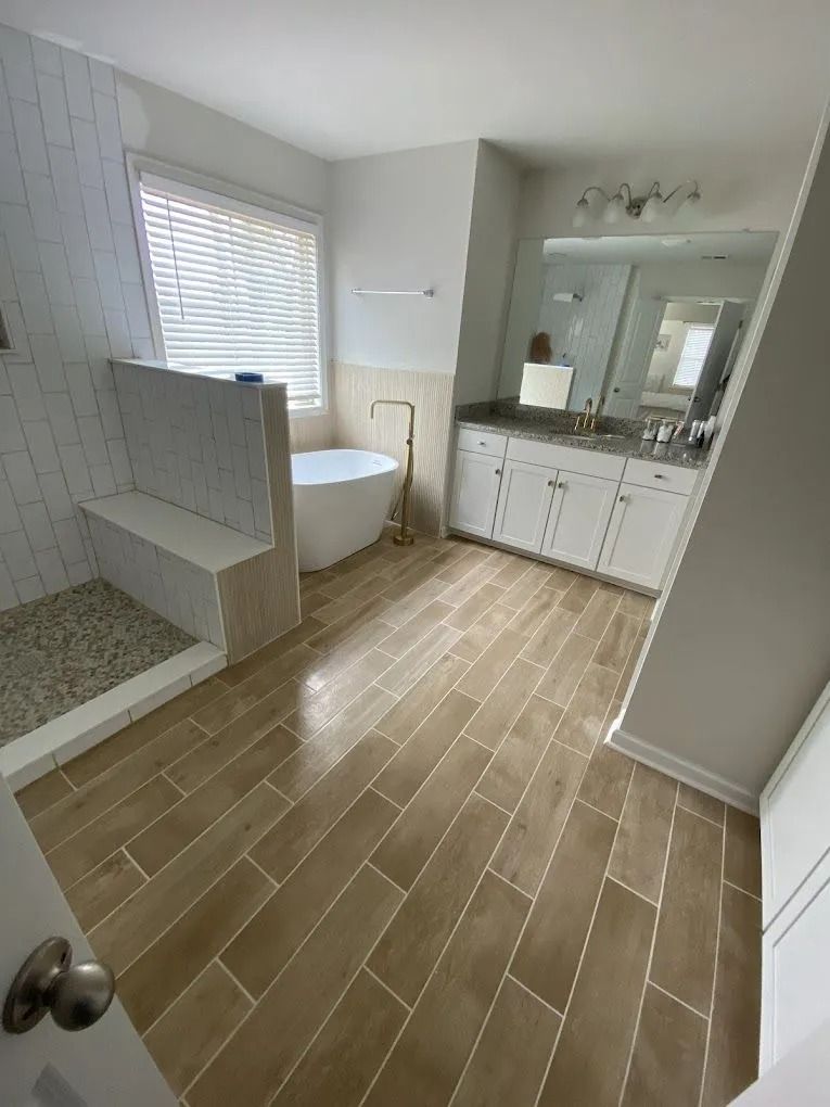 Bright bathroom with white tub, double vanity, tiled shower, and wood-look floor.