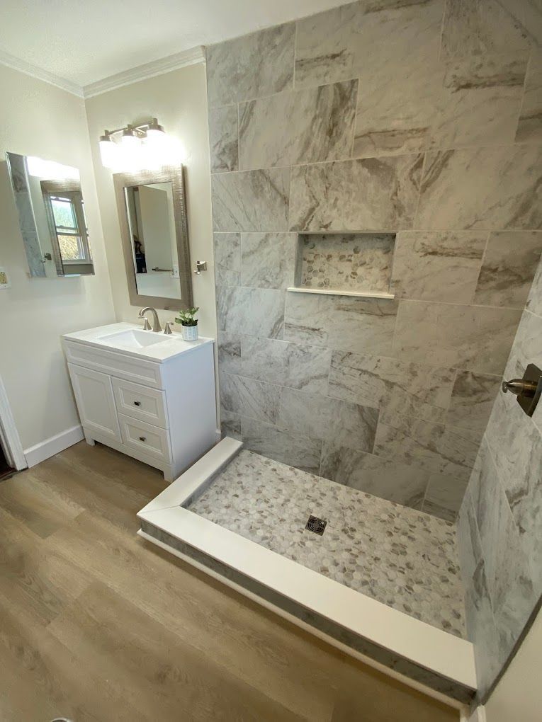 Bright modern bathroom with marble shower and vanity, white cabinetry, and wood-look floor