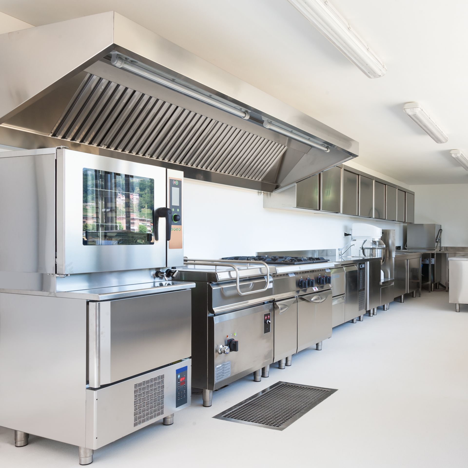 Commercial kitchen with stainless steel appliances, vent hood, and bright lighting.
