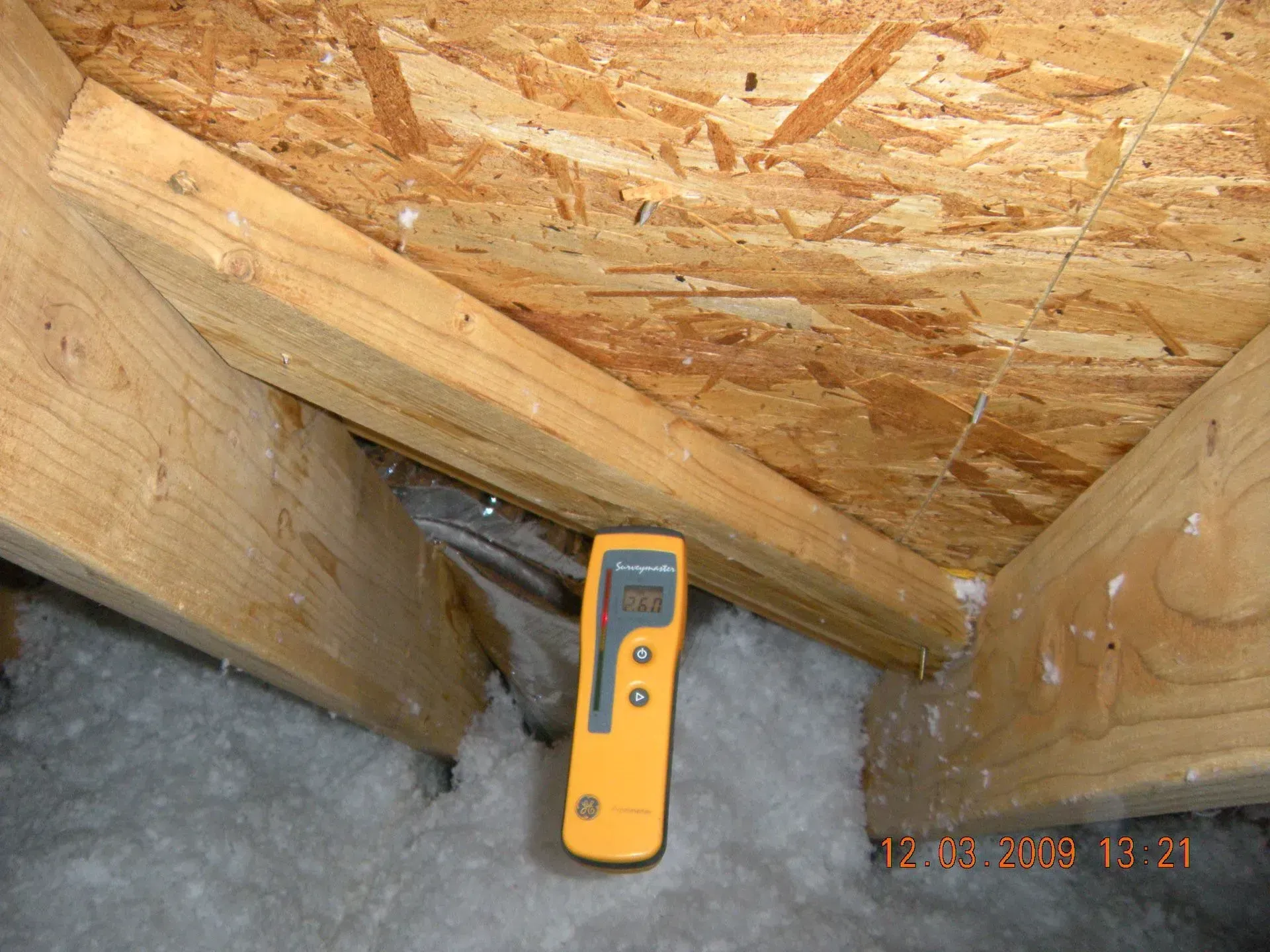 A thermometer is sitting on a wooden floor in an attic