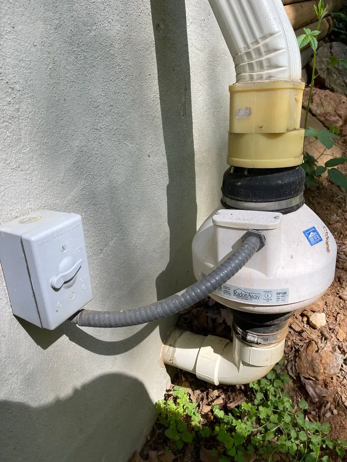 A white hose is attached to a white box on the side of a building.