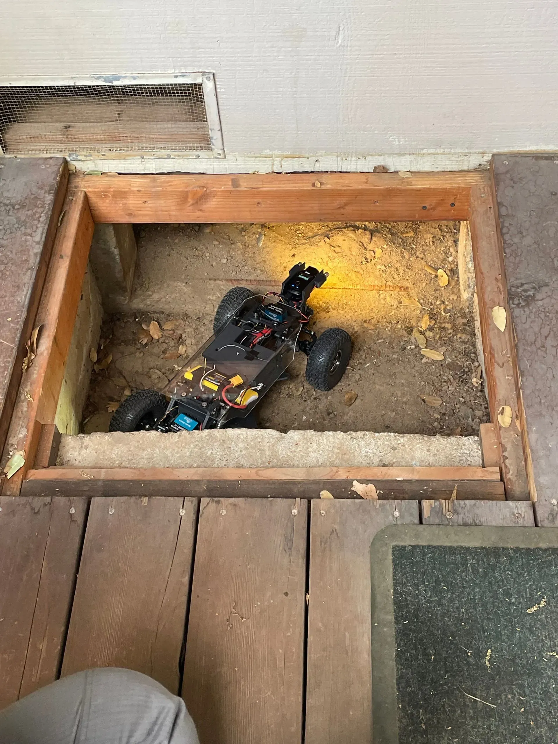 A remote control car is sitting in a hole in the floor.