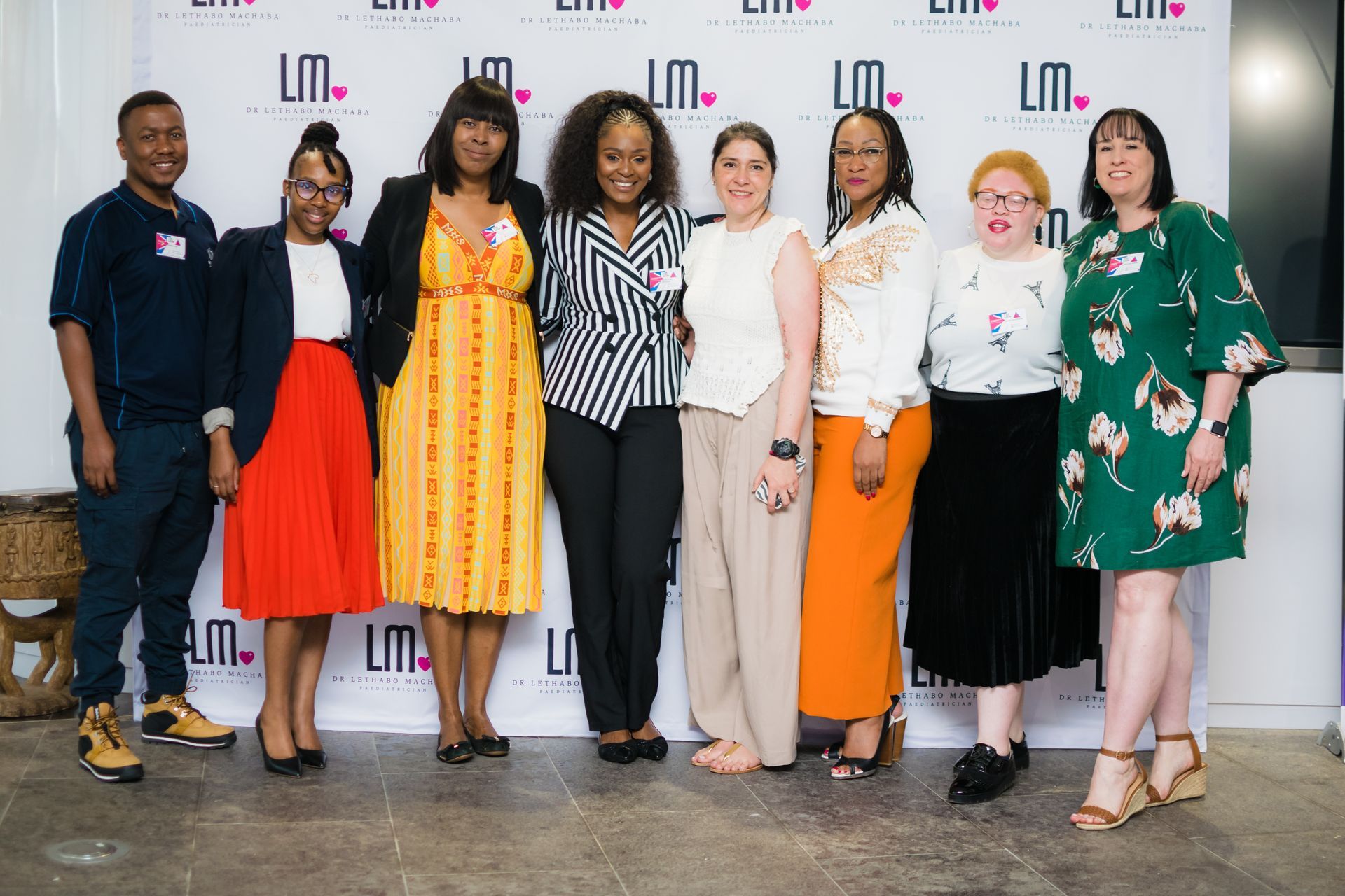 Group of people posing in front of a logo backdrop. Diverse attire and skin tones.