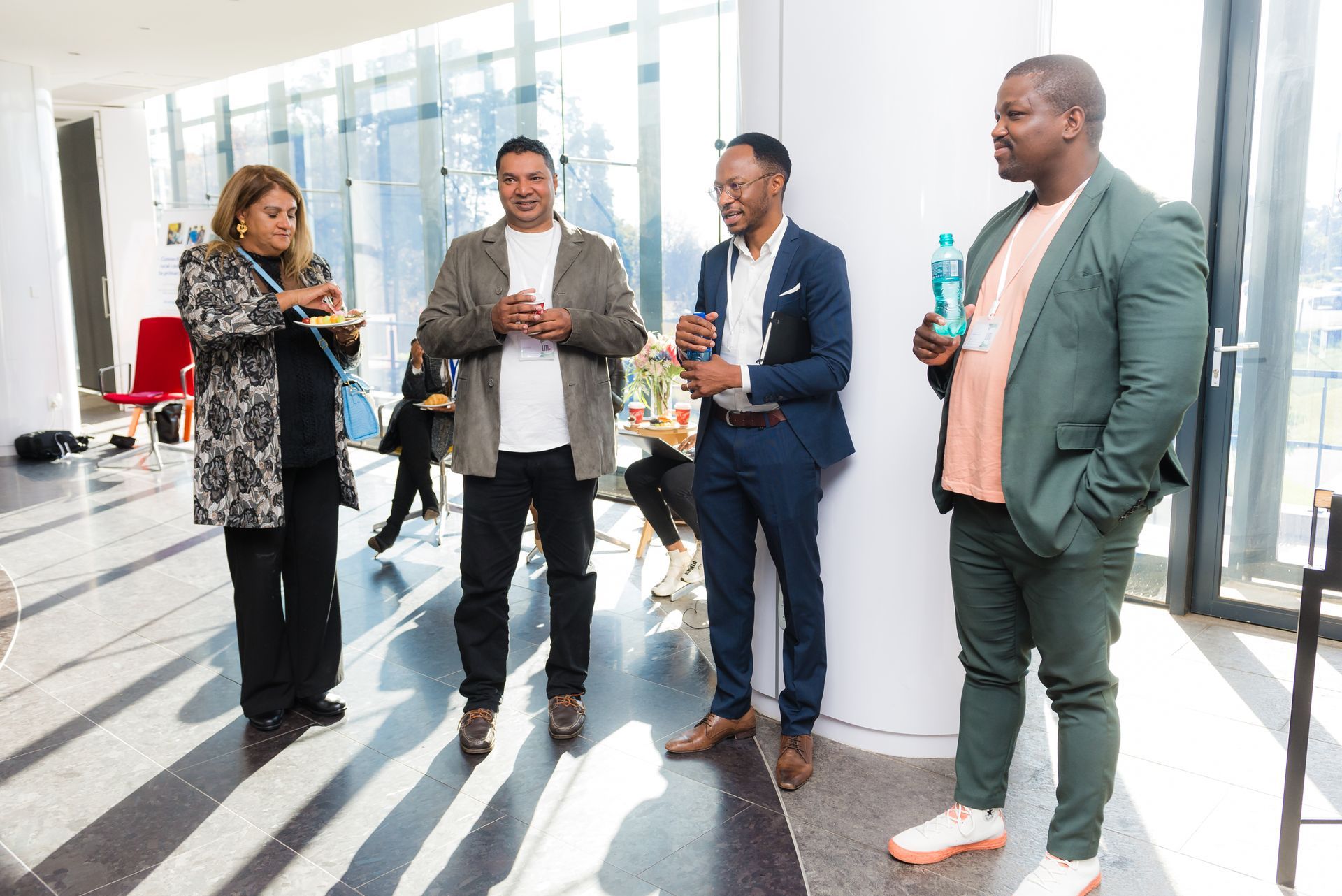 Four people in a bright room: two men and two women. They are conversing and holding drinks.