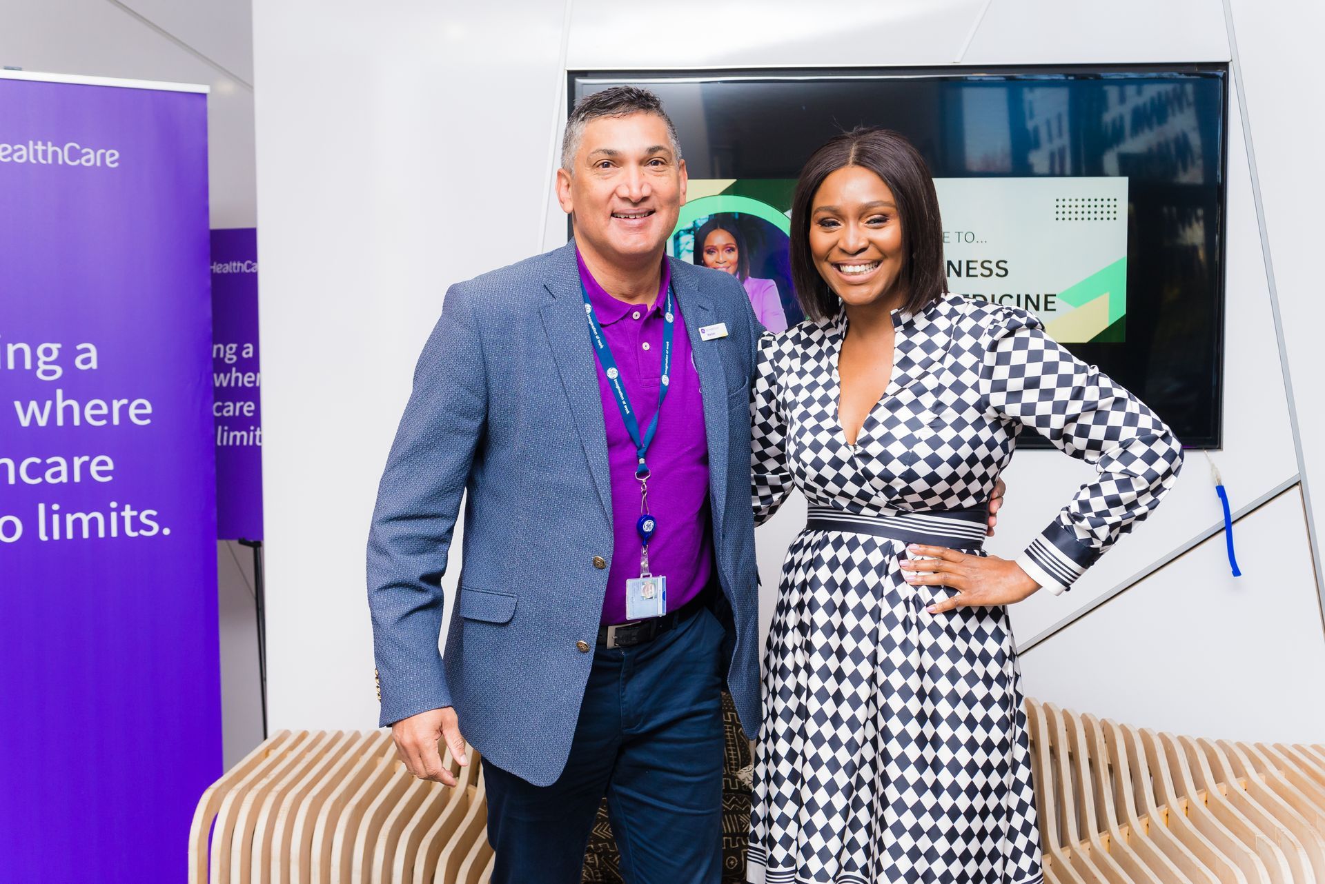 Man and woman posing, indoors. Man in purple and blue, woman in black and white checkered jacket, smiling.