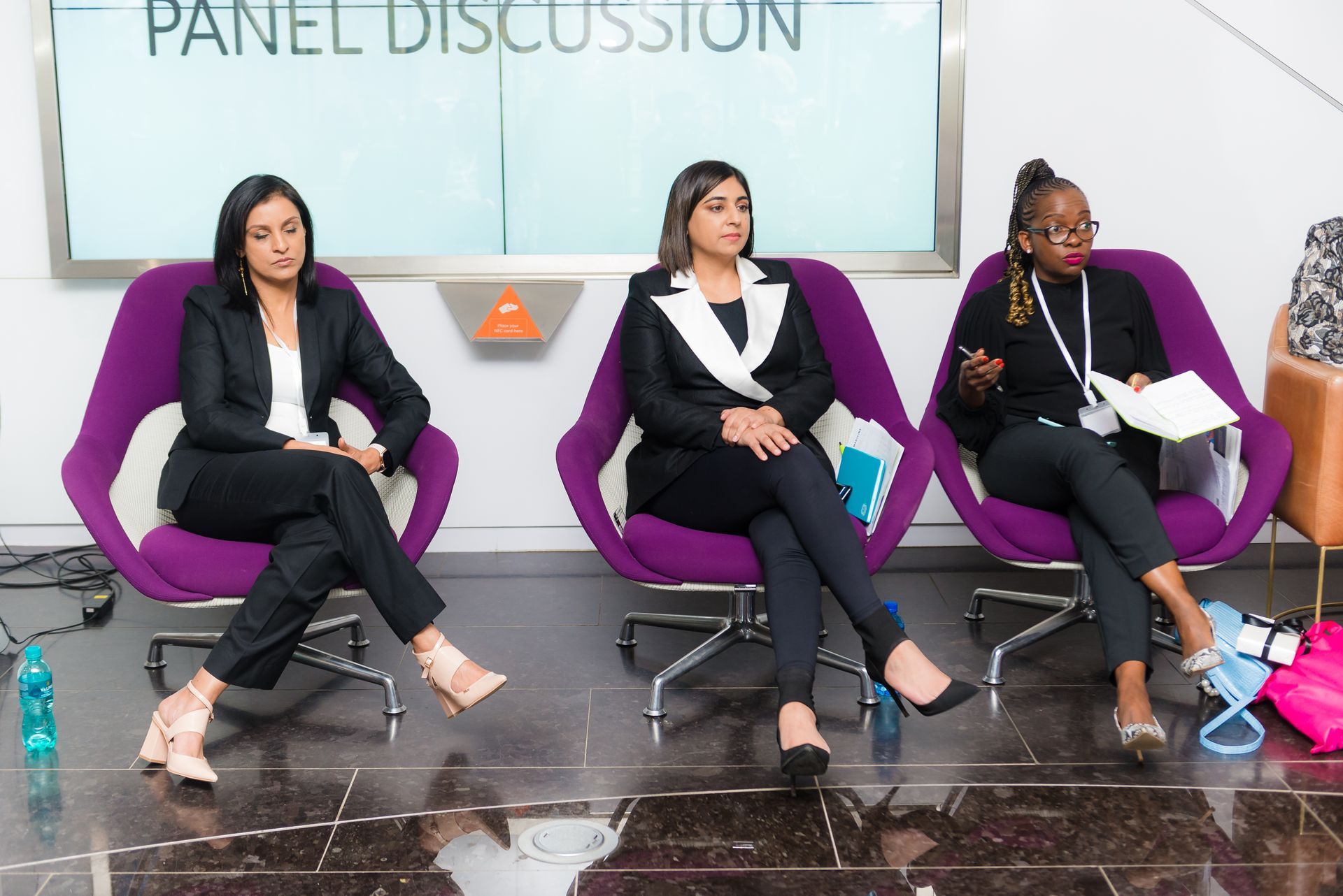 Panel discussion: Three women in business attire sit on purple chairs, engaging in conversation.