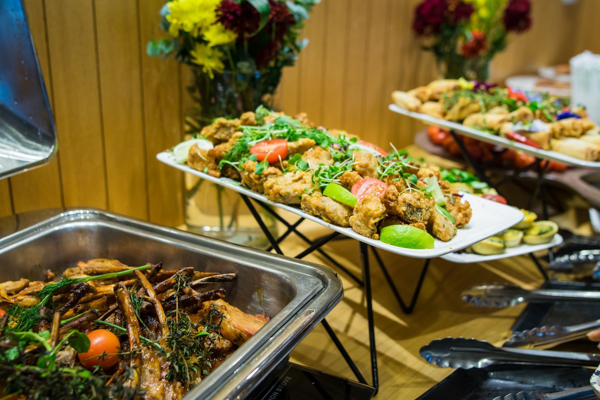 Buffet table with various dishes: fried food, vegetables, and floral arrangements.
