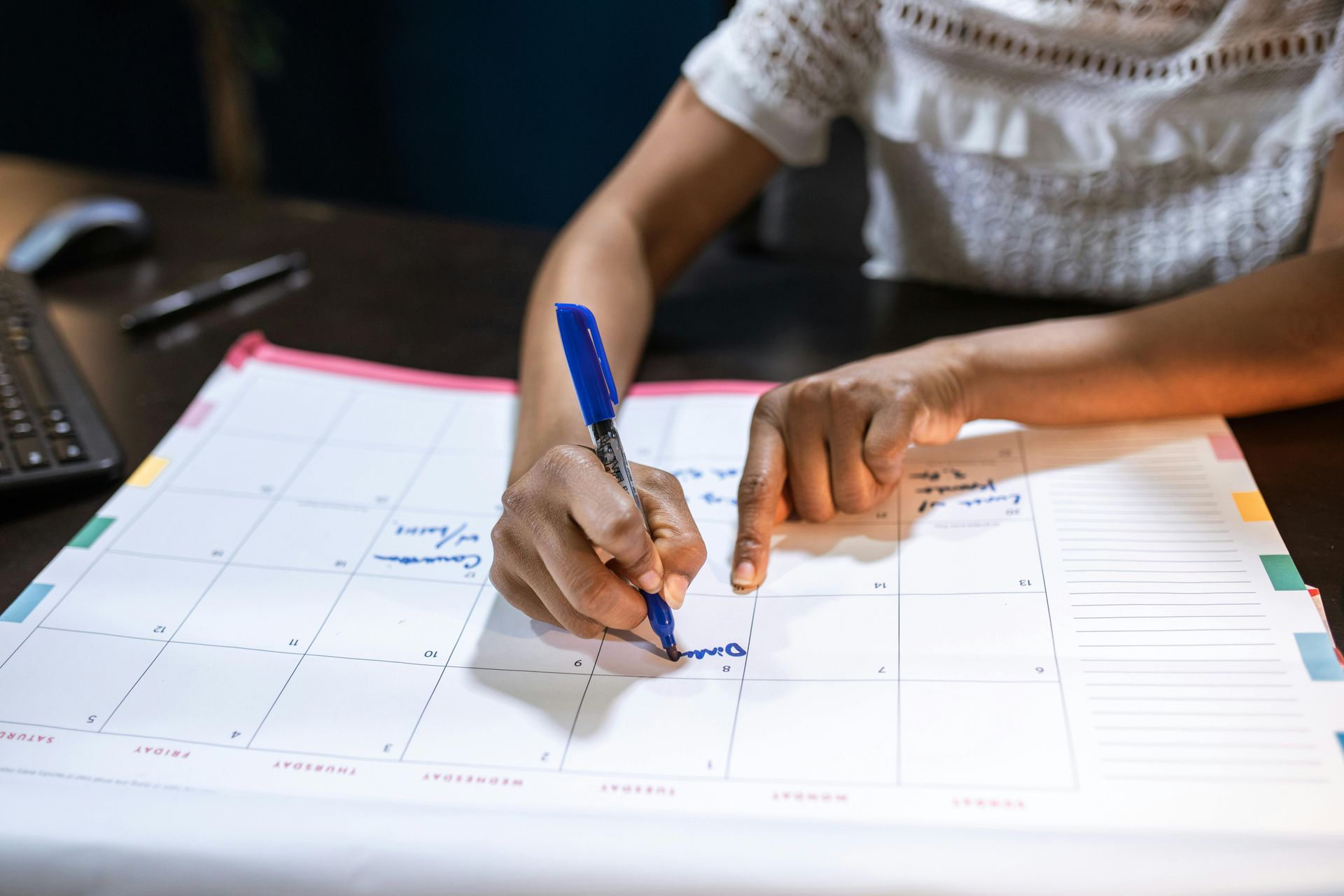 Person writing on a large calendar with a blue pen.