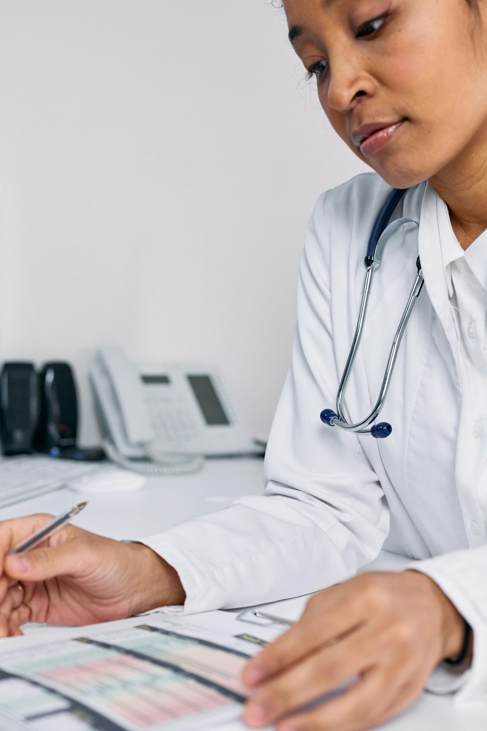 Doctor reviewing paperwork at a desk, wearing a stethoscope.
