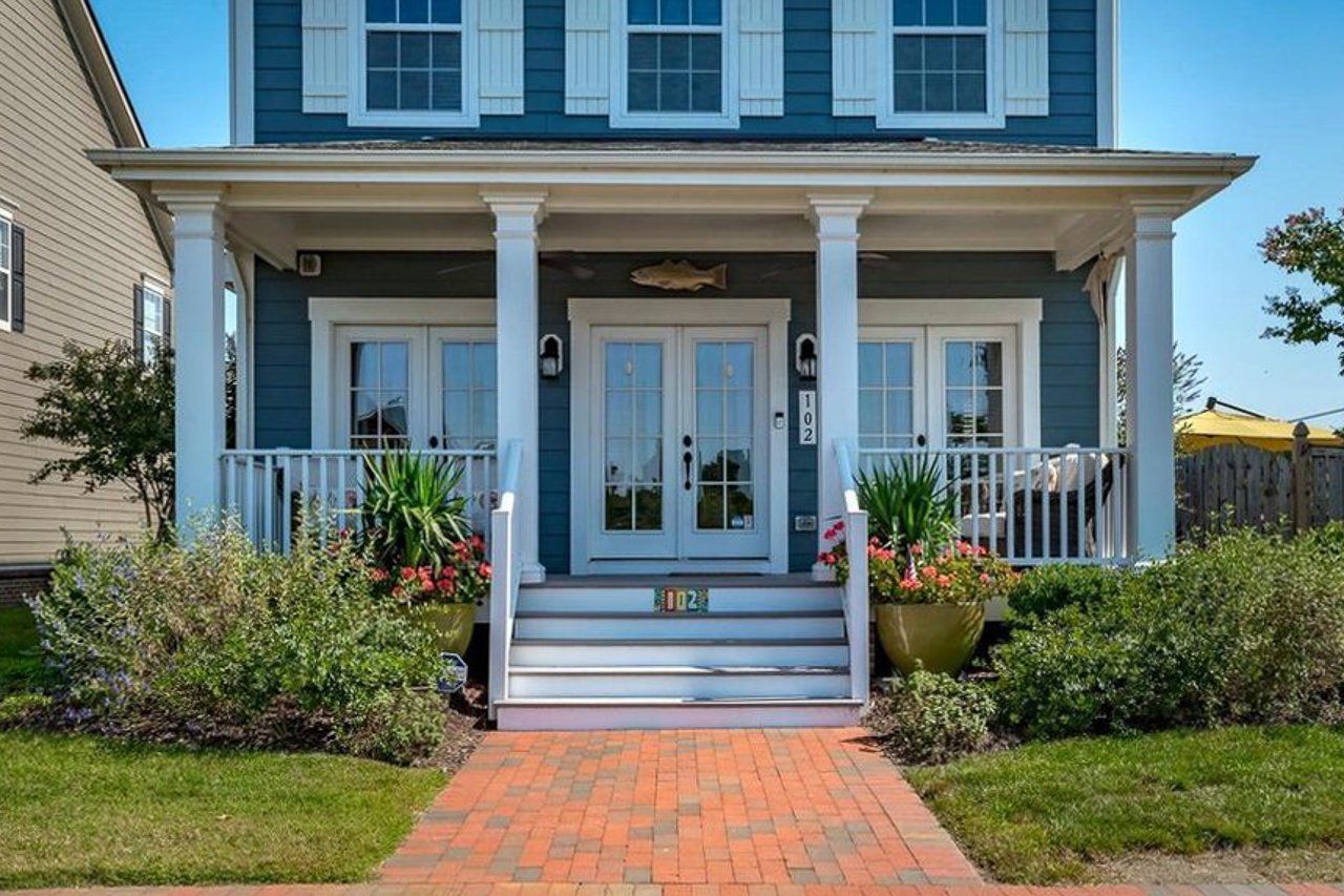 A blue house with white shutters and a brick walkway leading to it.