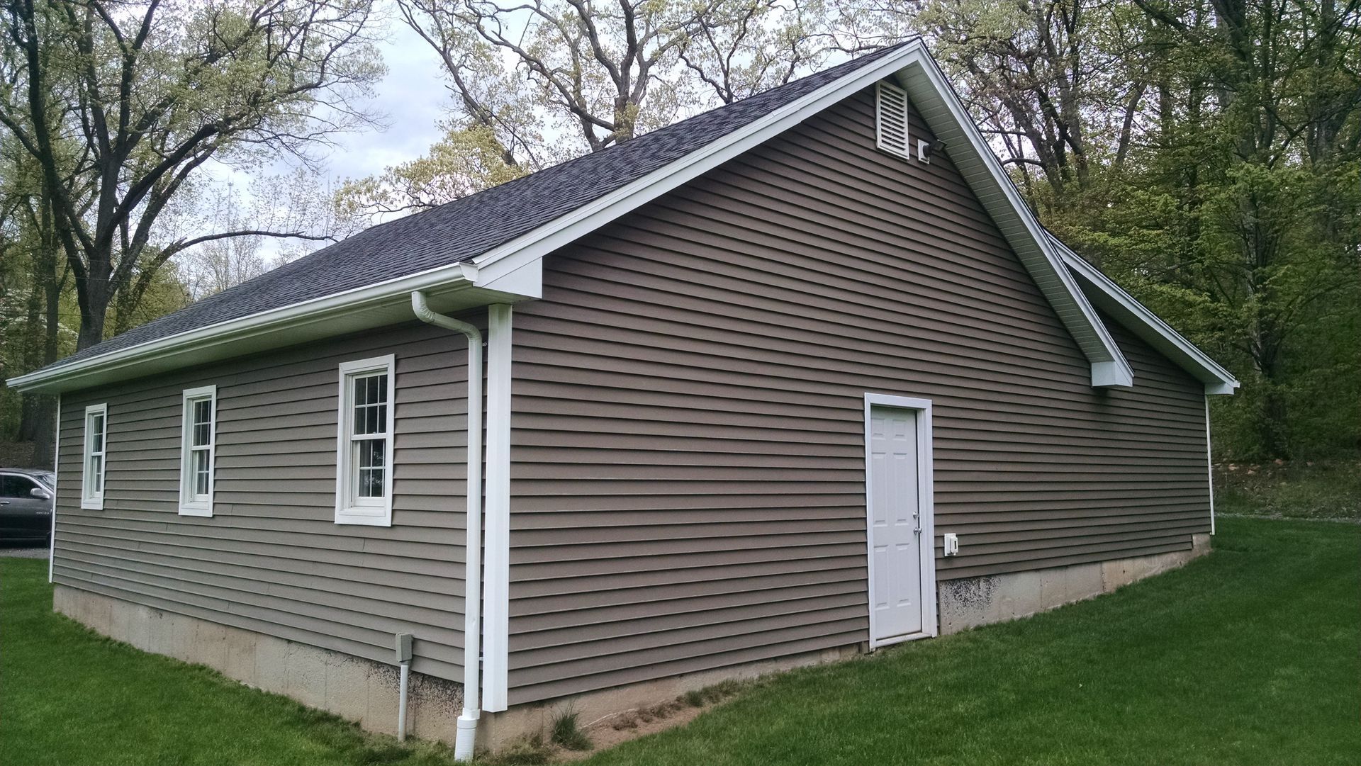 A house with a car parked in front of it and trees in the background.