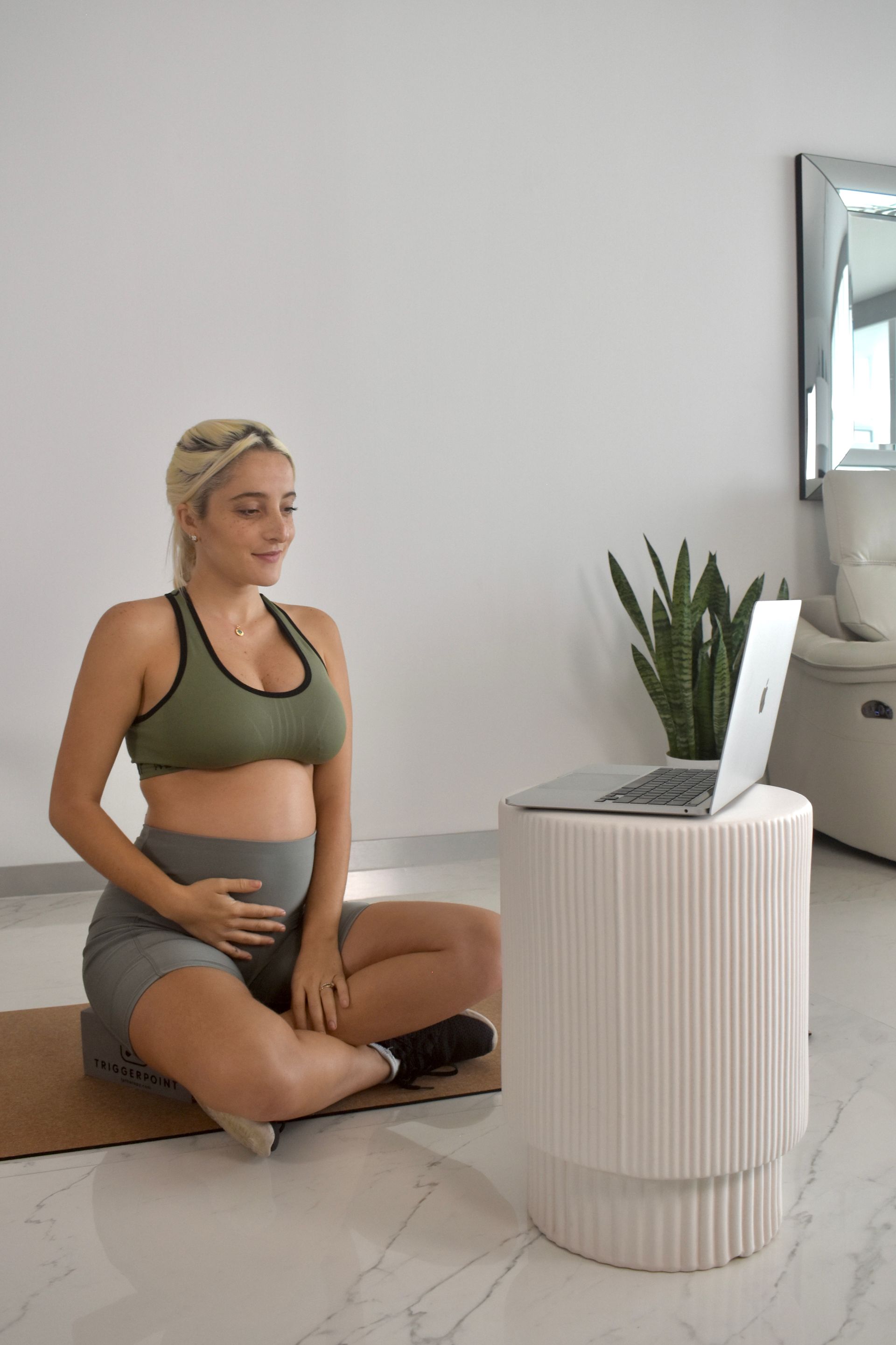 A pregnant woman is sitting on the floor in front of a laptop computer.