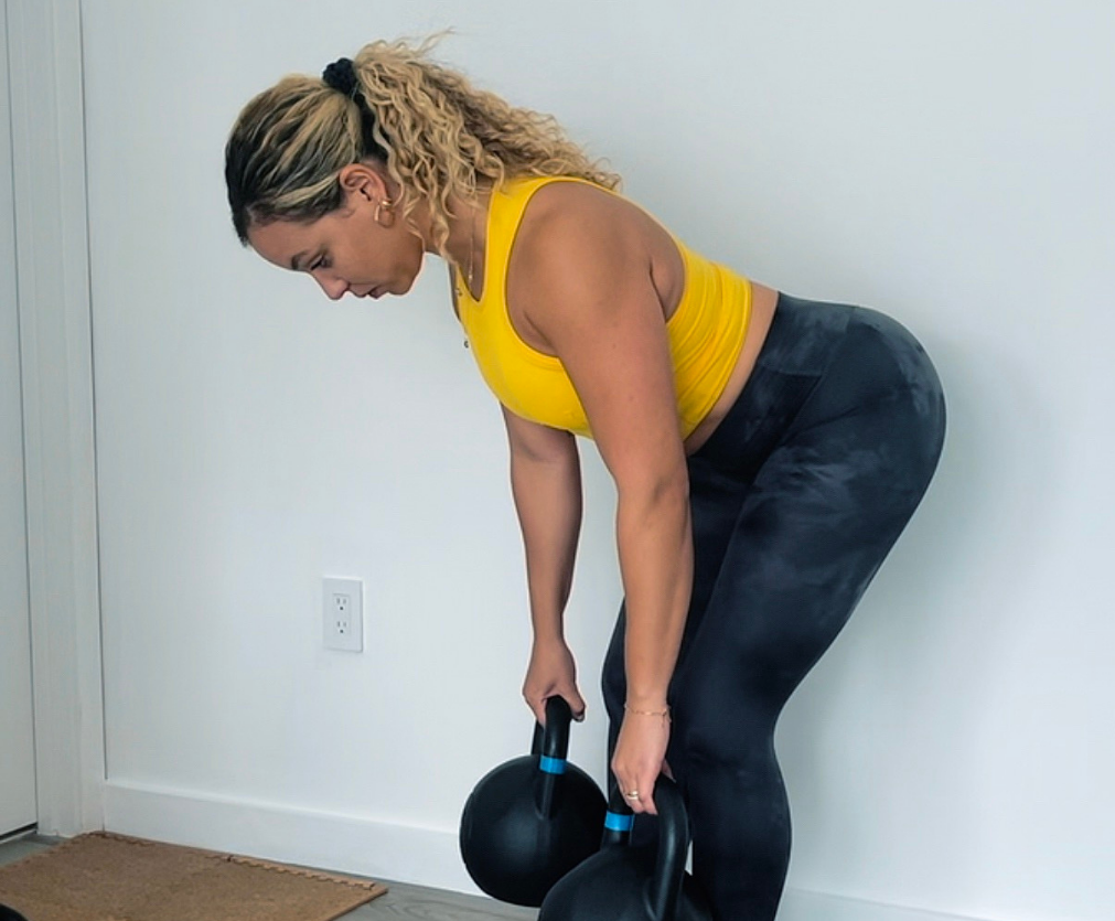 A woman in a yellow tank top is lifting a kettlebell.