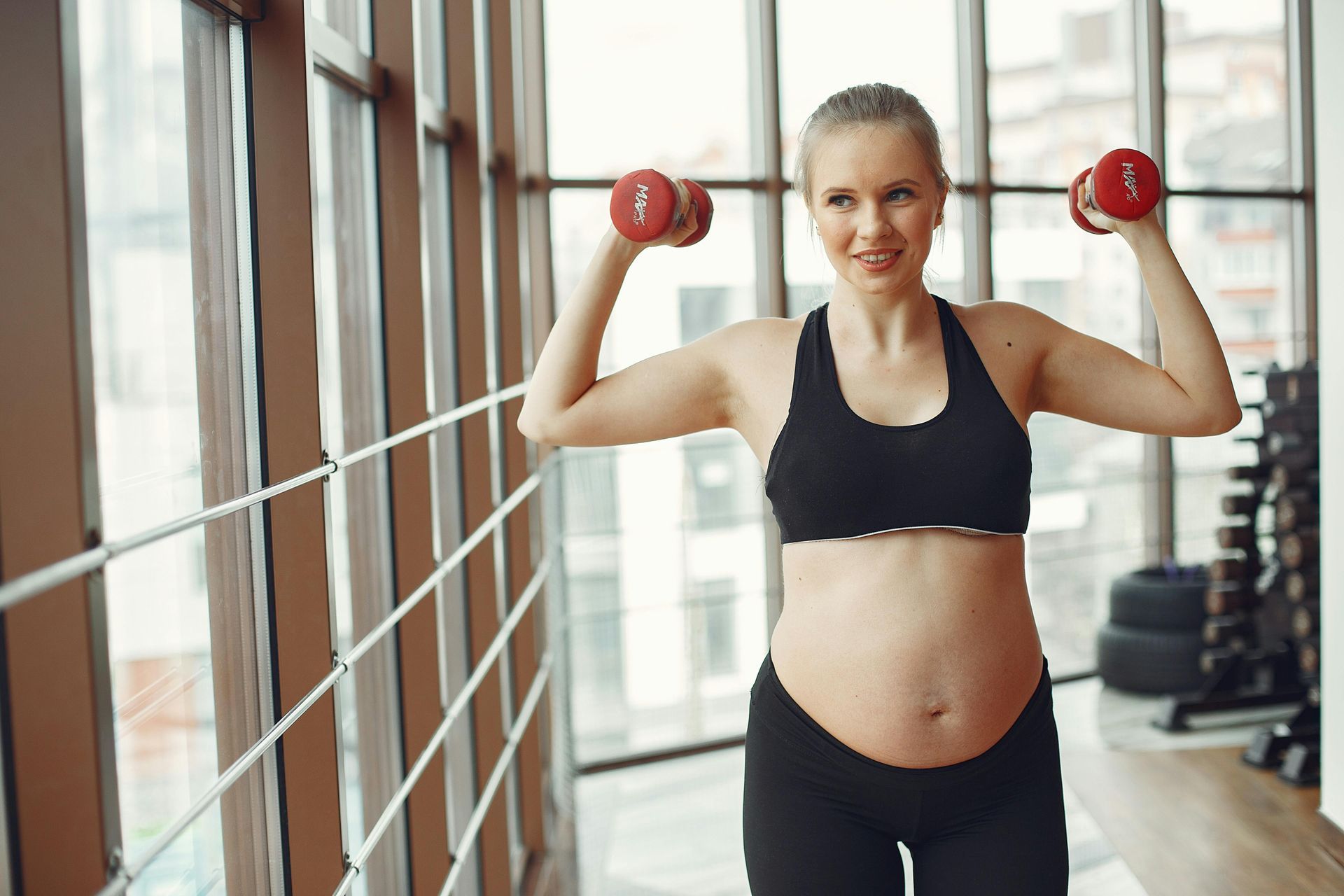 A pregnant woman is lifting dumbbells in a gym.