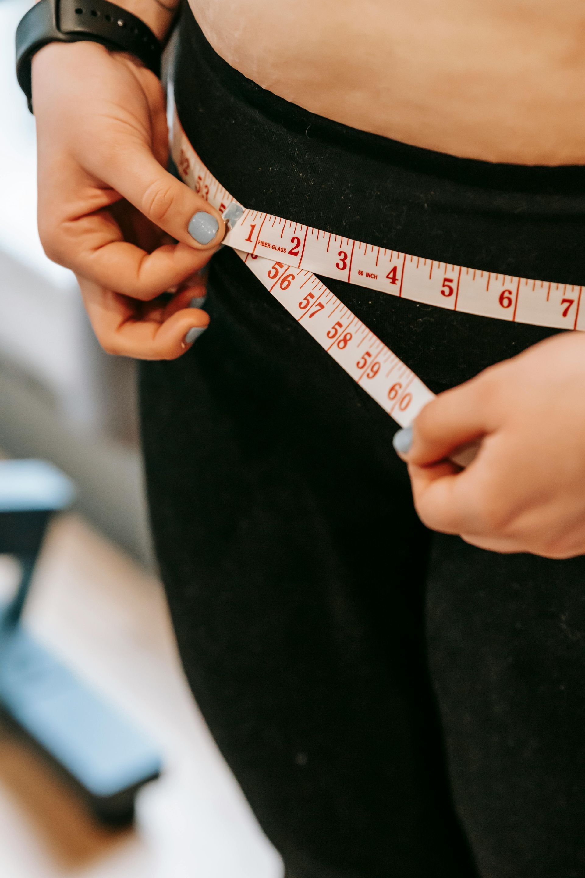 A woman is measuring her waist with a tape measure.