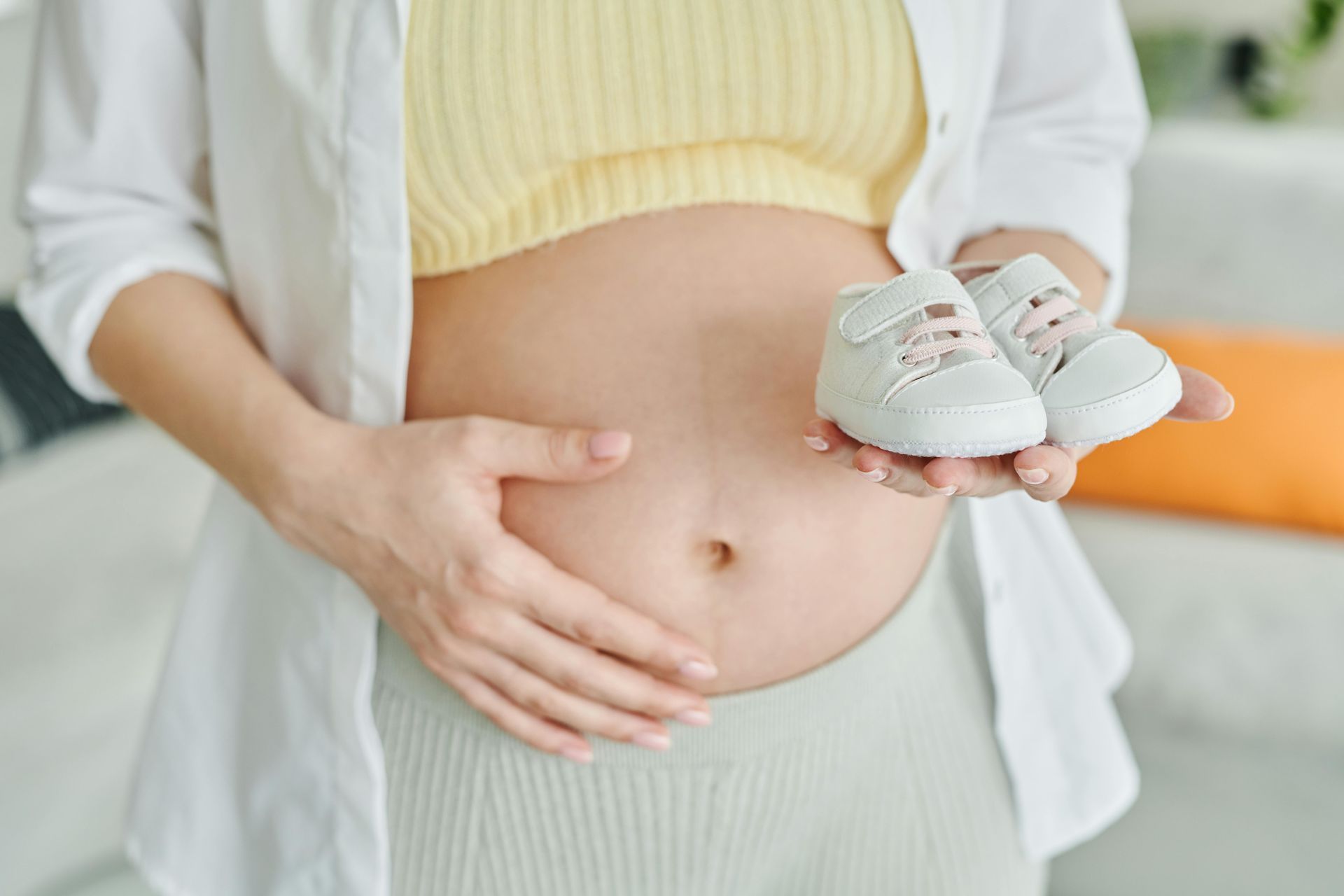 A pregnant woman is holding a pair of baby shoes in front of her belly.