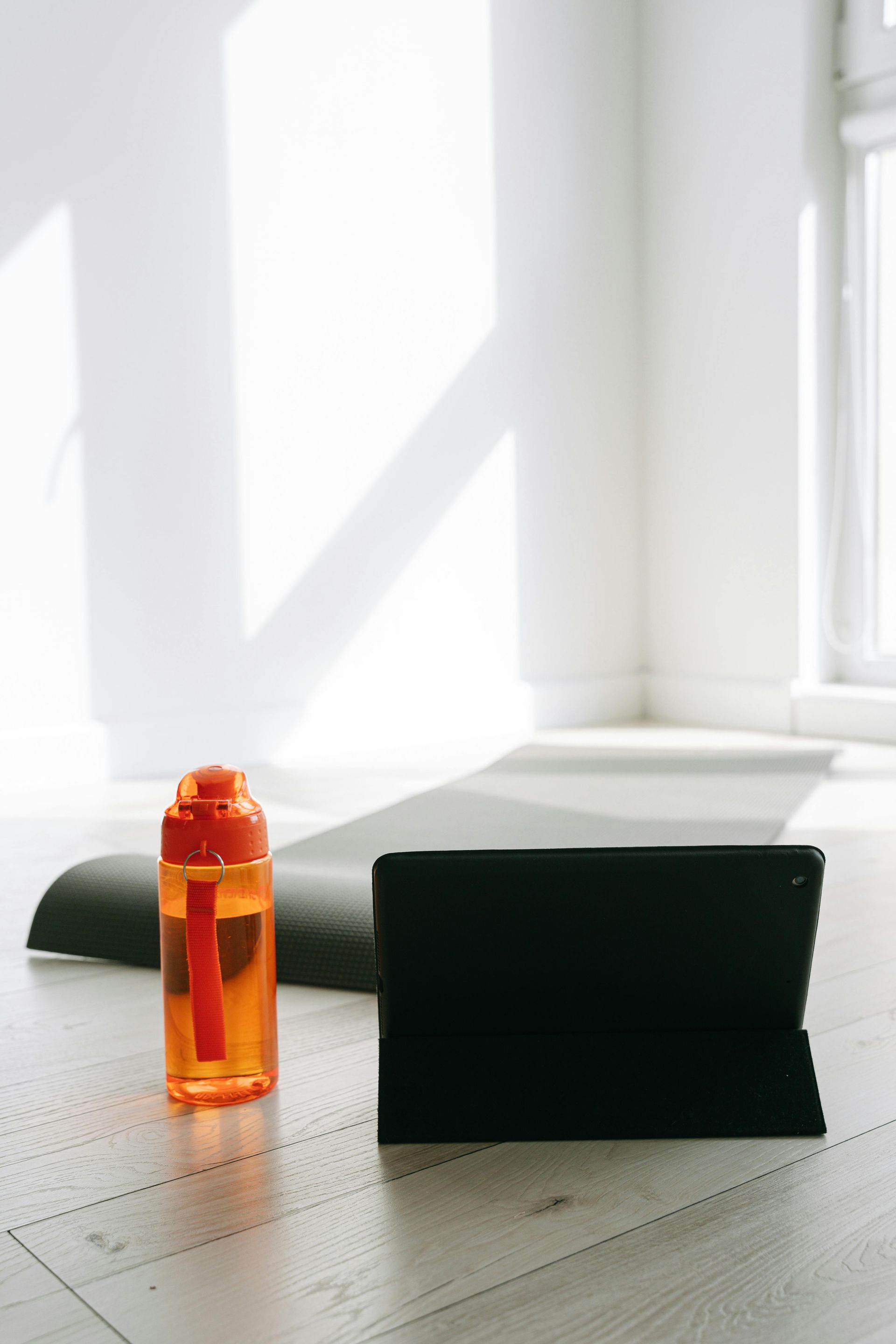 A water bottle and a tablet are on a yoga mat.