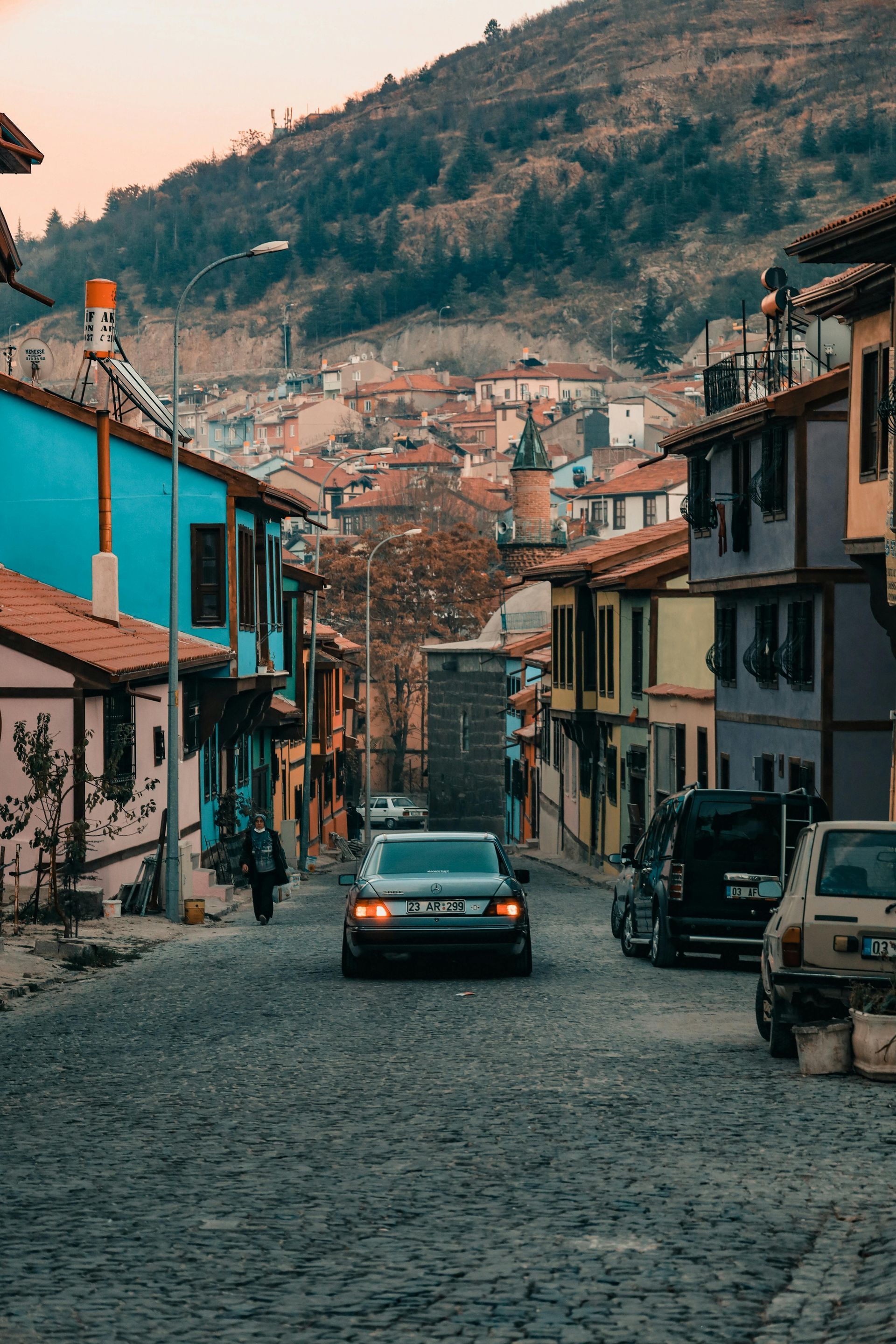 Cobblestone street in Turkish town; colorful buildings line road with a car driving towards viewer.