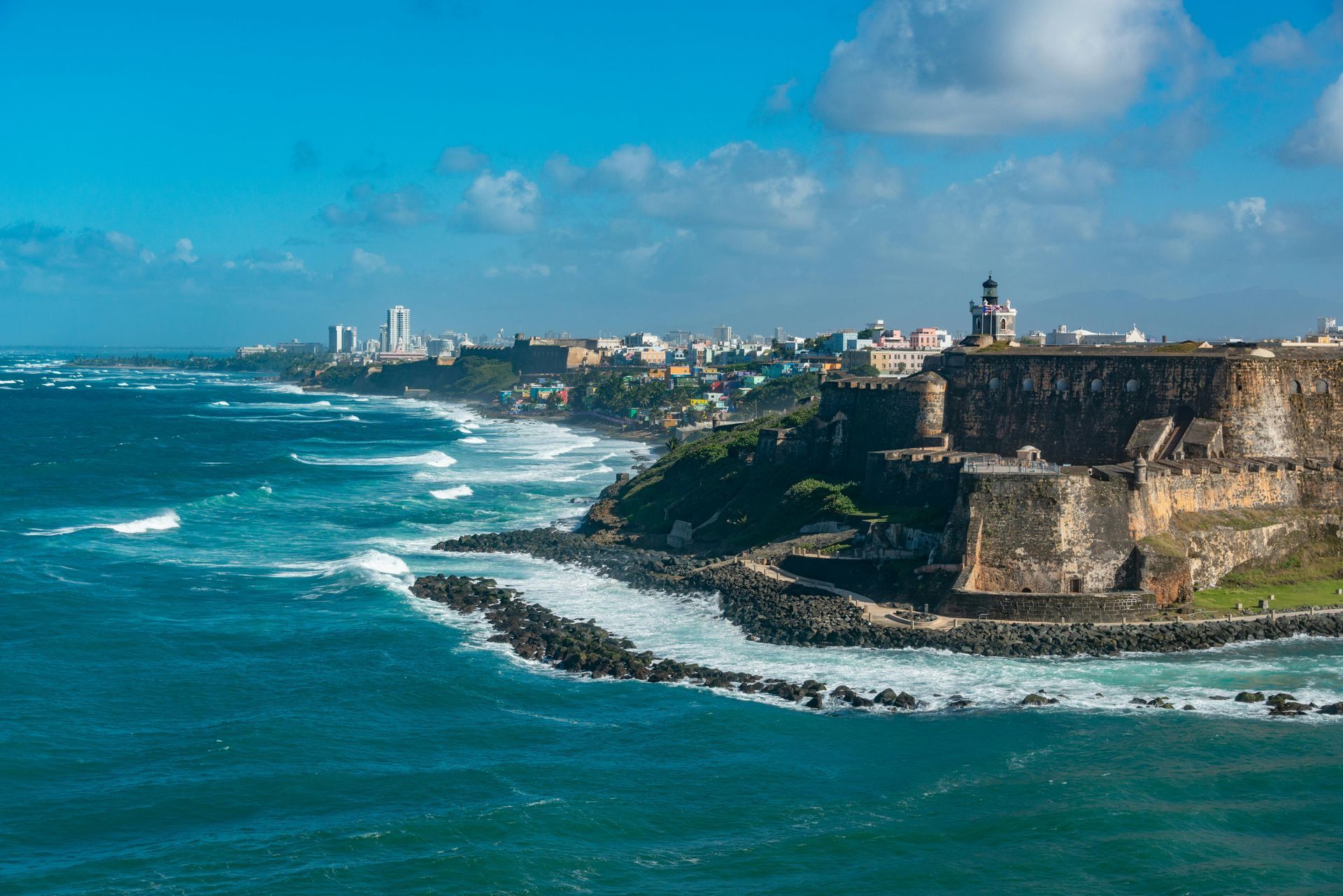Coastal view of San Juan, Puerto Rico. Fortress and city line the rocky shore with turquoise ocean.
