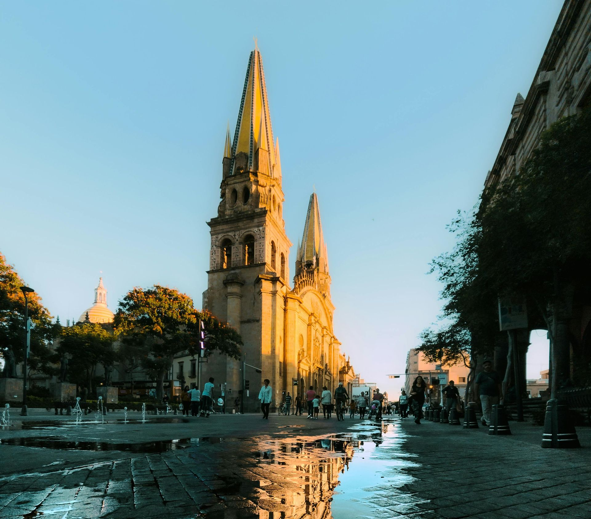 Cathedral in Guadalajara, Mexico, with reflections in puddles on cobblestone street, blue sky.