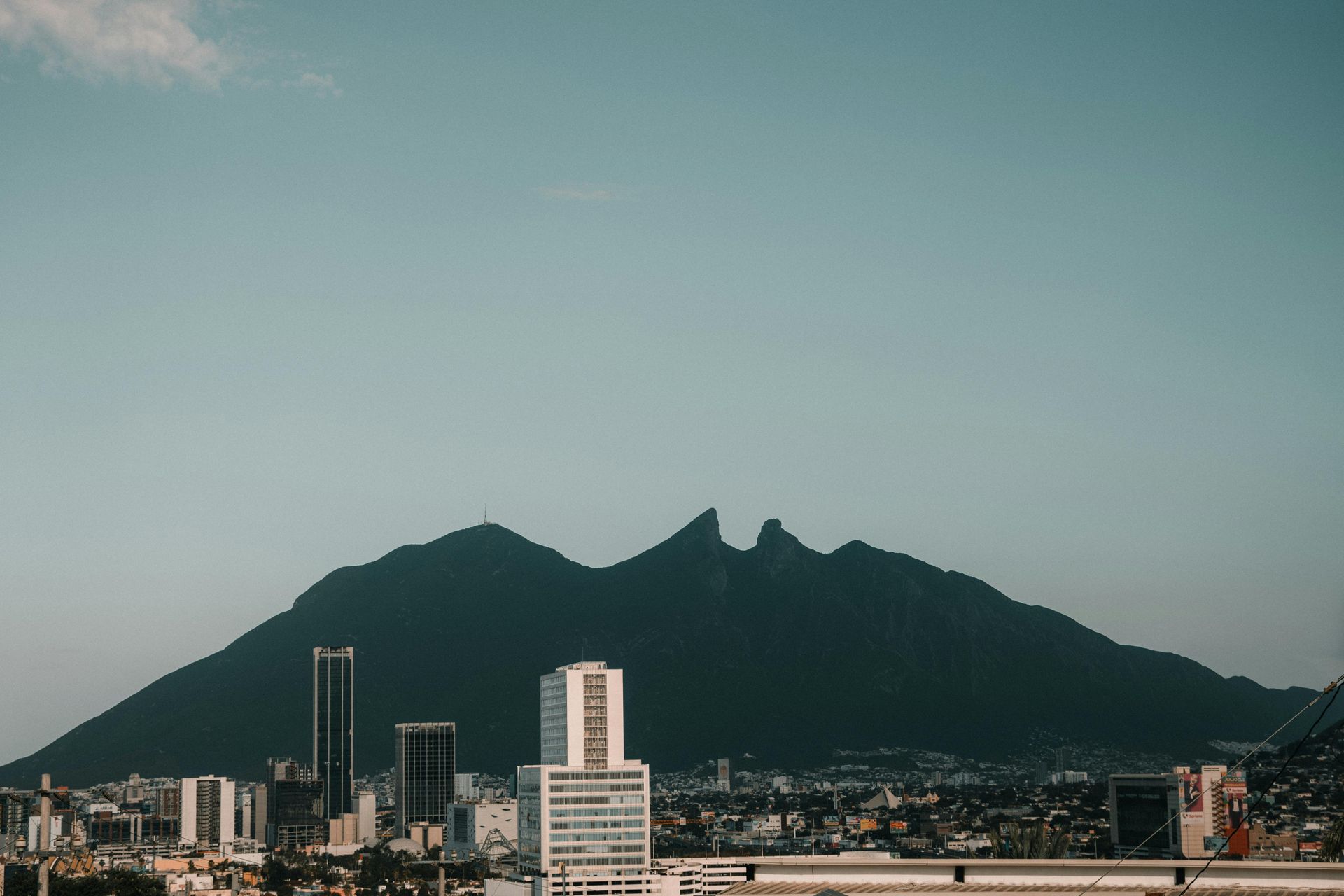 City skyline in front of a large mountain under a clear, blue sky.