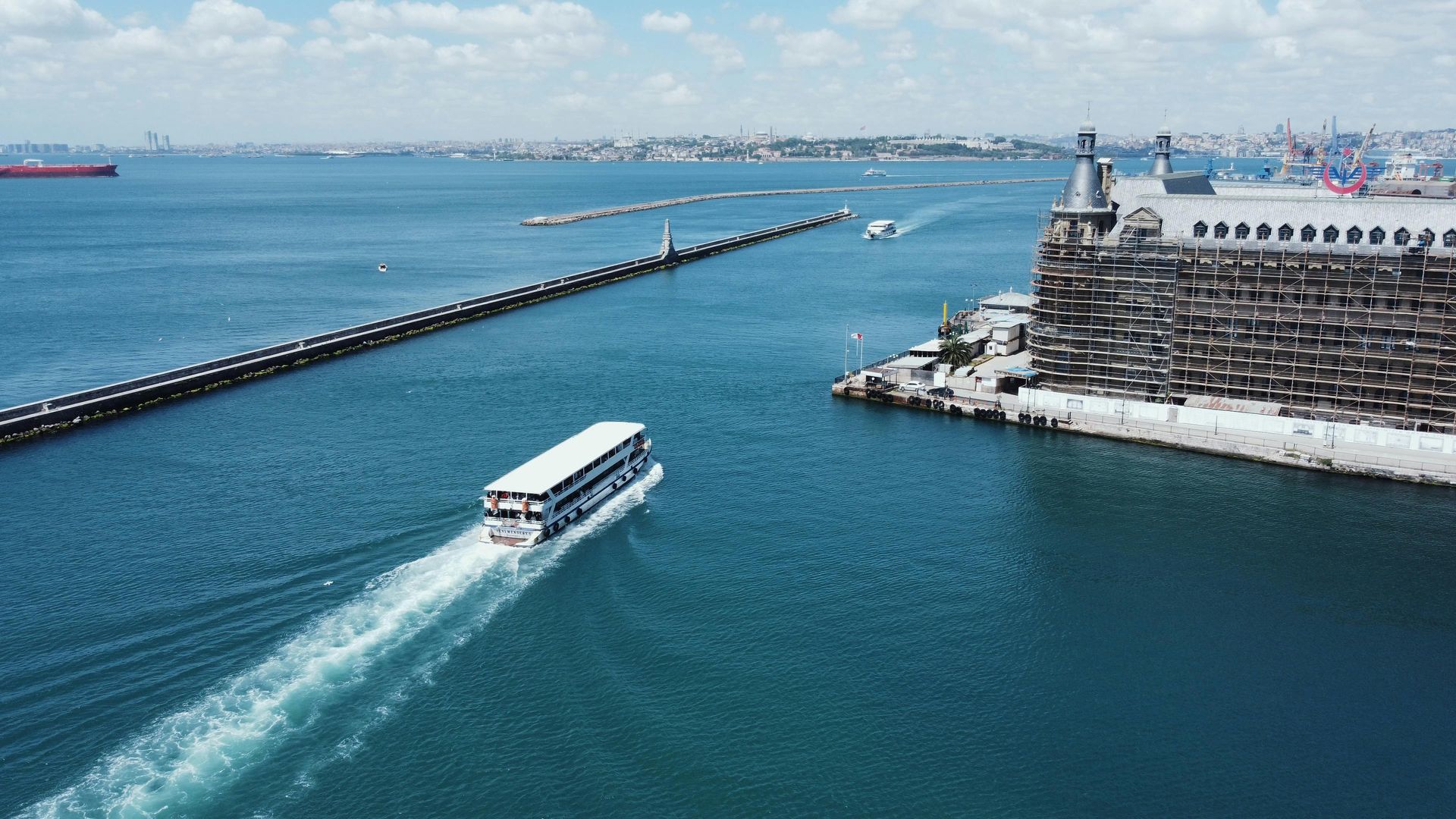A boat moves through blue water near a historic brick building and pier under a clear sky.
