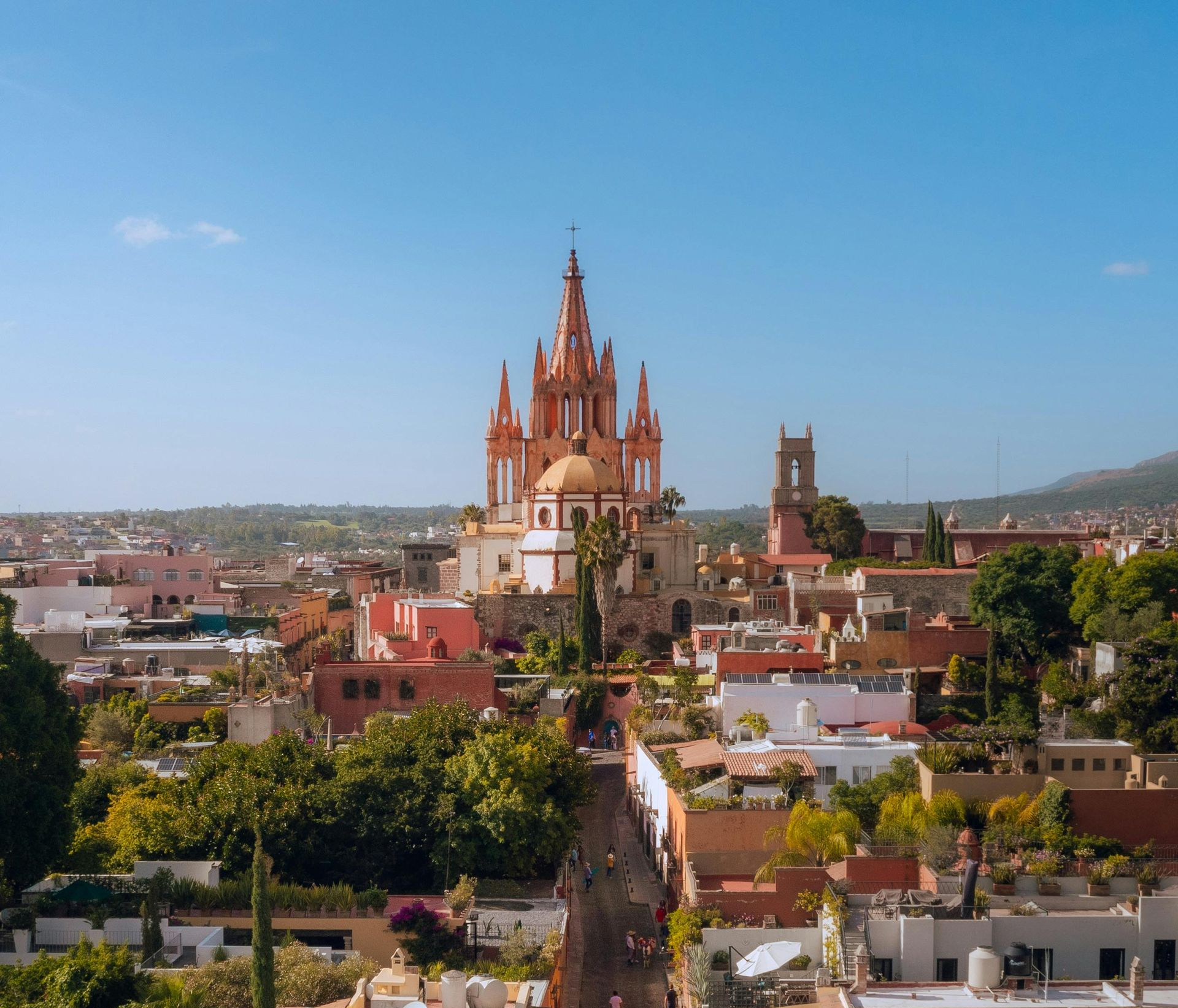 Rooftop view of pink-colored church in San Miguel de Allende, Mexico, surrounded by town buildings under a blue sky.