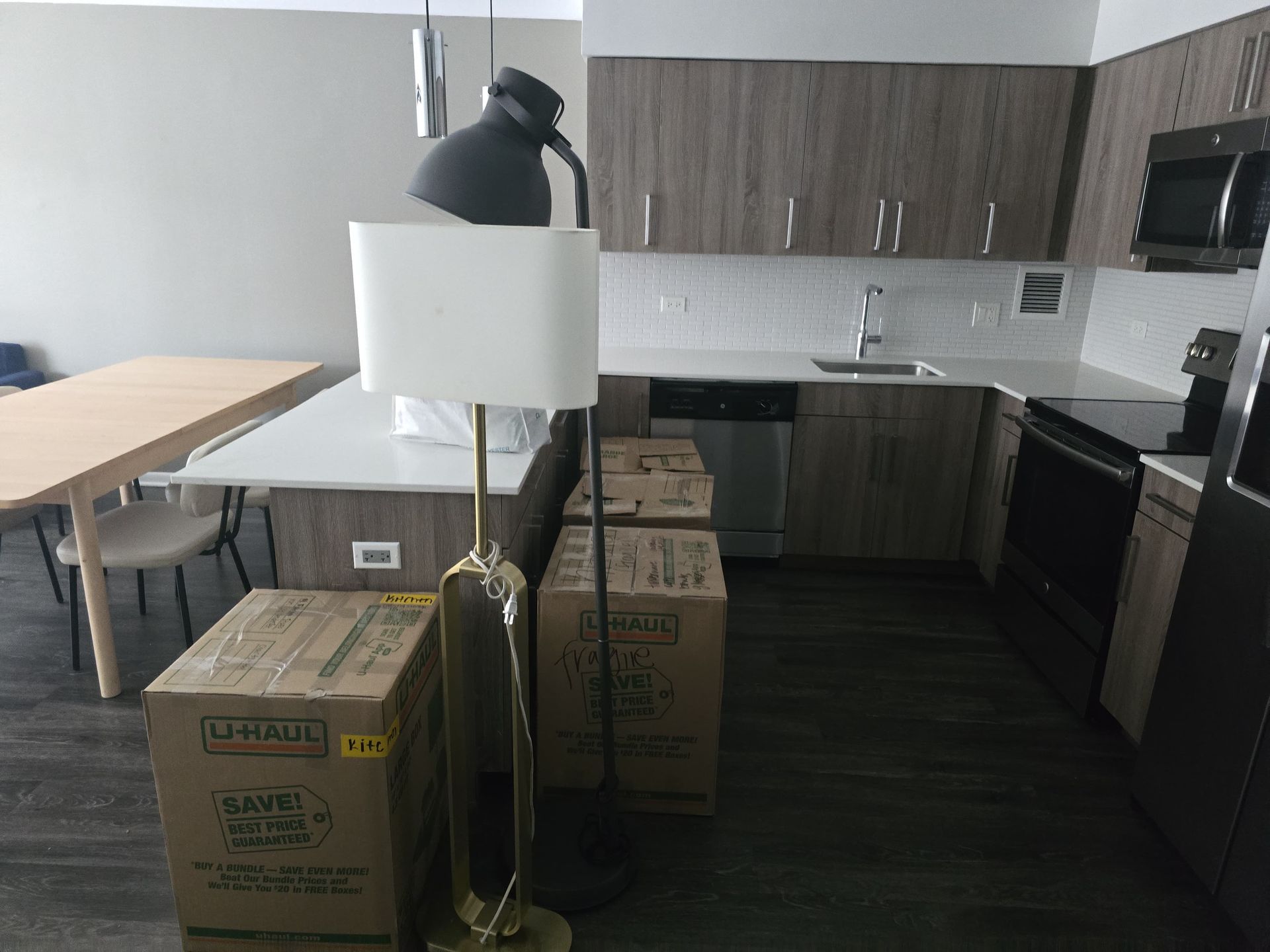 A kitchen area featuring wood cabinets, stainless steel appliances, a dining table, and several cardboard moving boxes.