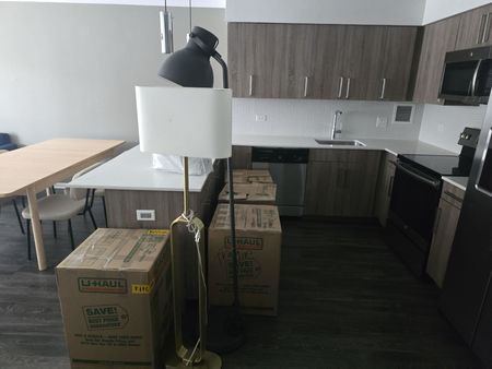 A kitchen area featuring wood cabinets, stainless steel appliances, a dining table, and several cardboard moving boxes.