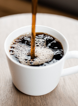 A cup of coffee is being poured into a cup on a table.