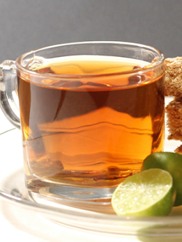 A cup of tea is on a saucer next to a slice of lime.