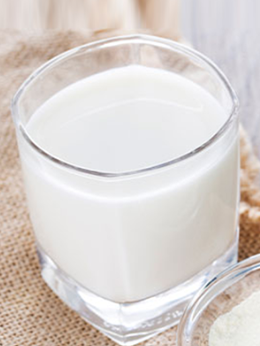 A glass of milk is sitting on a table next to a bowl of milk powder.