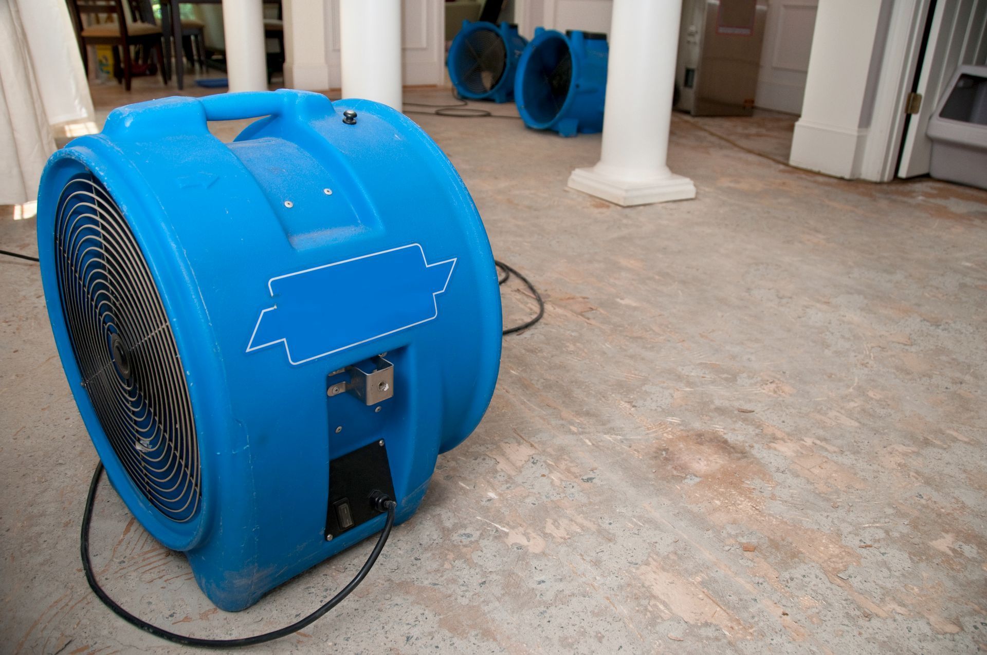 Room with industrial air movers drying a bare floor during water damage restoration work.