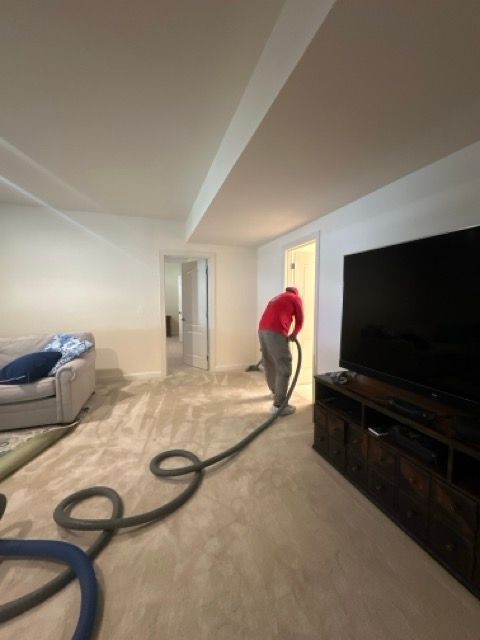 A man in a red shirt is using a vacuum cleaner in a living room