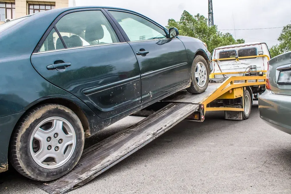 Green car being towed onto a flatbed tow truck in a parking lot.  — Mission Truck Training in Mountain Creek, QLD
